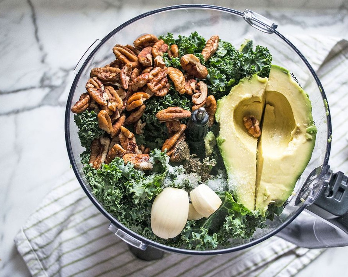 step 1 Add Kale (3 cups), Avocado (1/2), Unsalted Raw Pecans (1/2 cup), Grated Parmesan Cheese (1/3 cup), Garlic (2 cloves), juice of Lemon (1), Sea Salt (1/2 tsp) and Freshly Ground Black Pepper (1/4 tsp) to the bowl of a food processor. Process on high for 15-20 seconds, stopping to scrape down the sides and add Water (4 Tbsp) until the pesto reaches preferred consistency. Taste and add more seasonings if needed.
