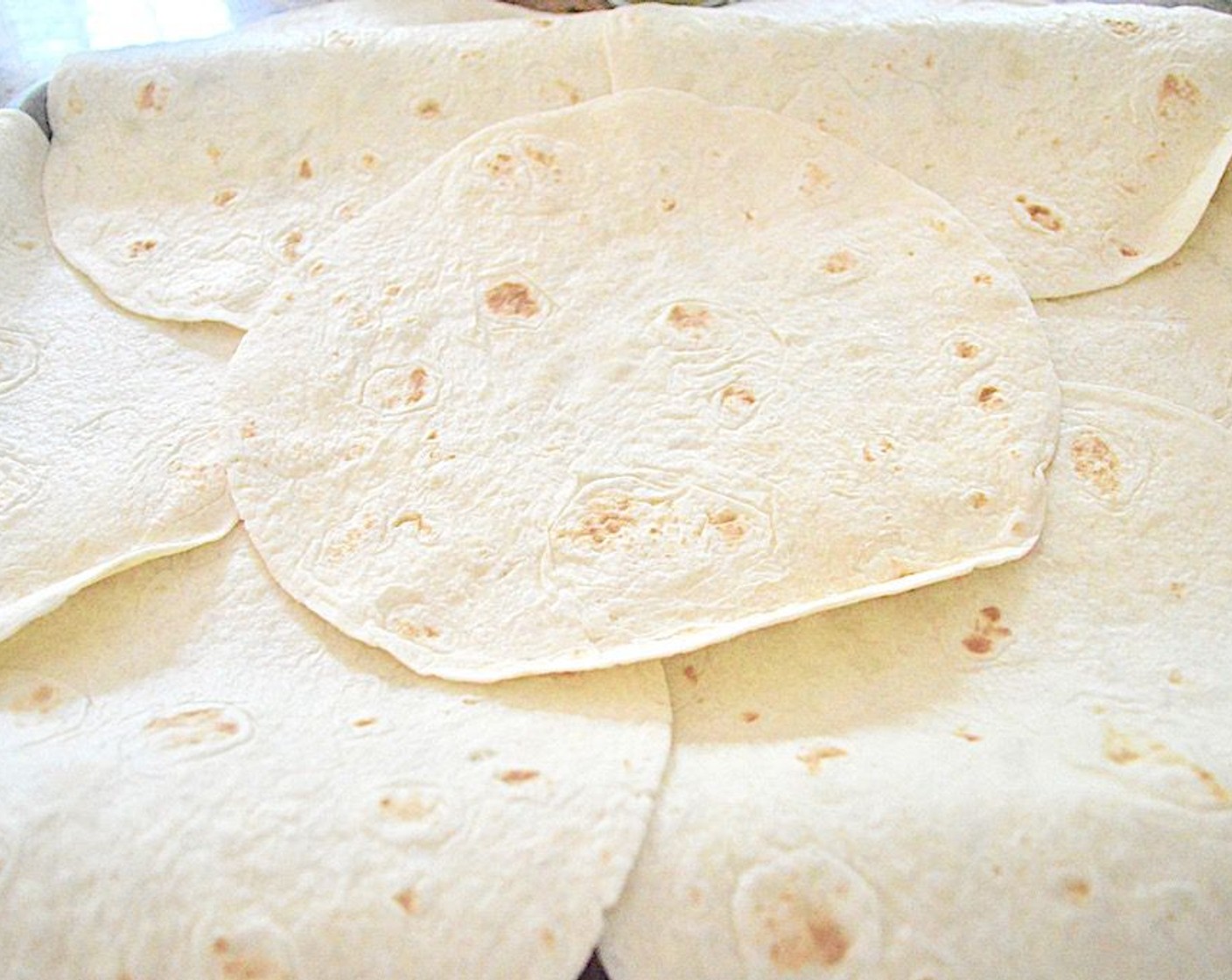 step 6 Take Flour Tortillas (7). Place 6 of them around the edge of the sheet tray with almost half of each tortilla hanging over the edge. In the tray the sides should all be connected. Then place another tortilla in the center so that there is a solid tortilla base.