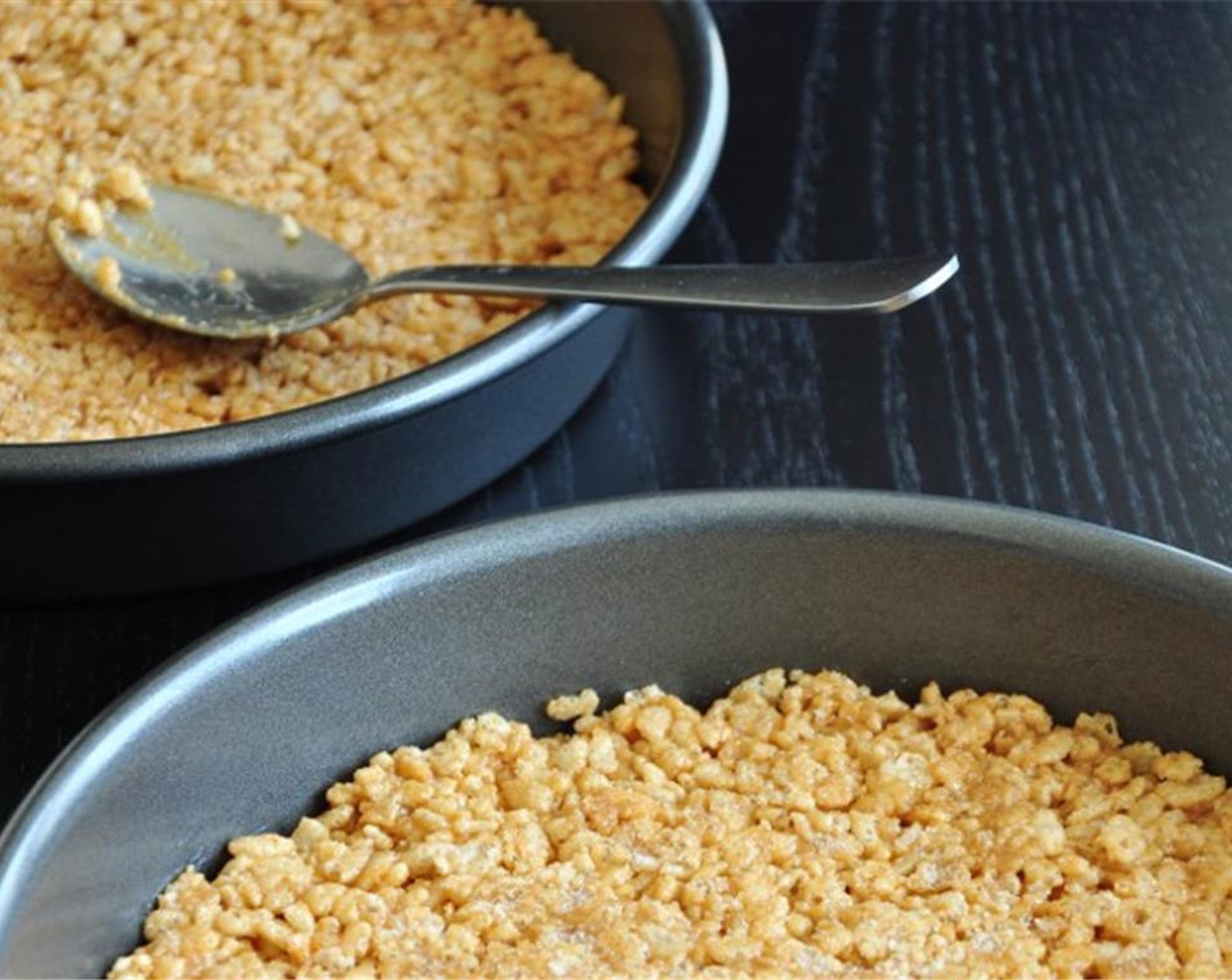 step 3 Butter two  9-inch round cake pans. Divide the mixture into two even portions and press firmly to the bottom of each cake pan by using the back of a regular-sized spoon.