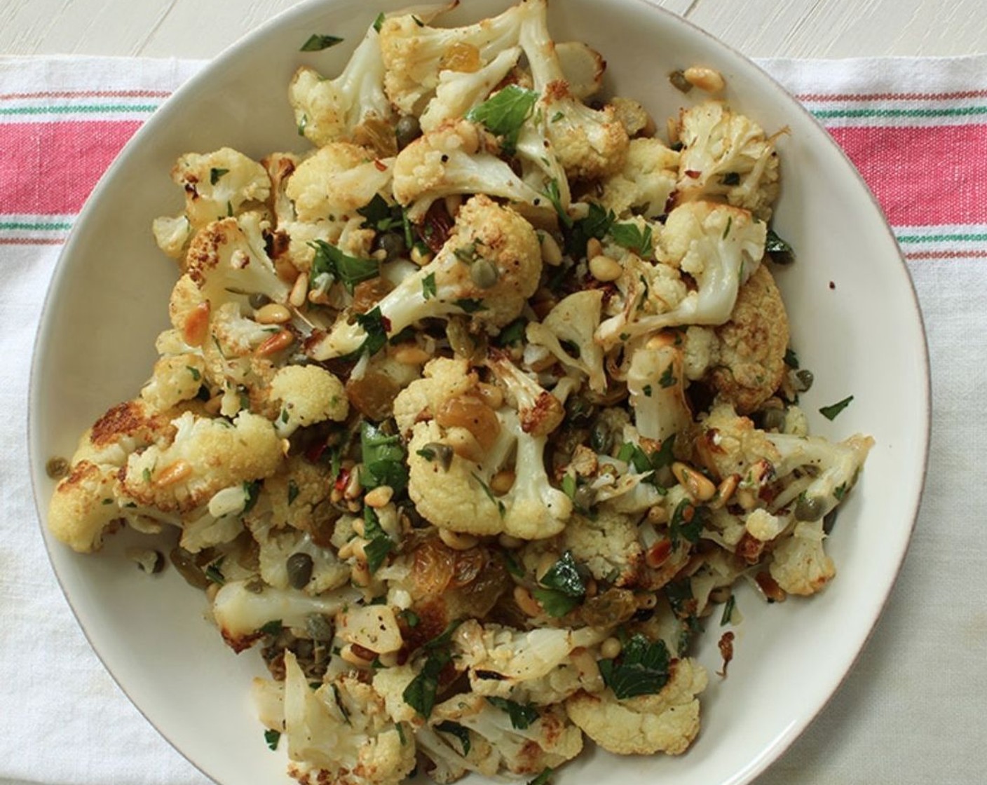 step 7 When the cauliflower is done, add the caper mixture, toasted pine nuts, Fresh Parsley (1/4 cup), and Crushed Red Pepper Flakes (1/4 tsp) to the sheet pan. Toss well, sprinkle generously with additional salt, then transfer to a shallow dish or platter and serve.