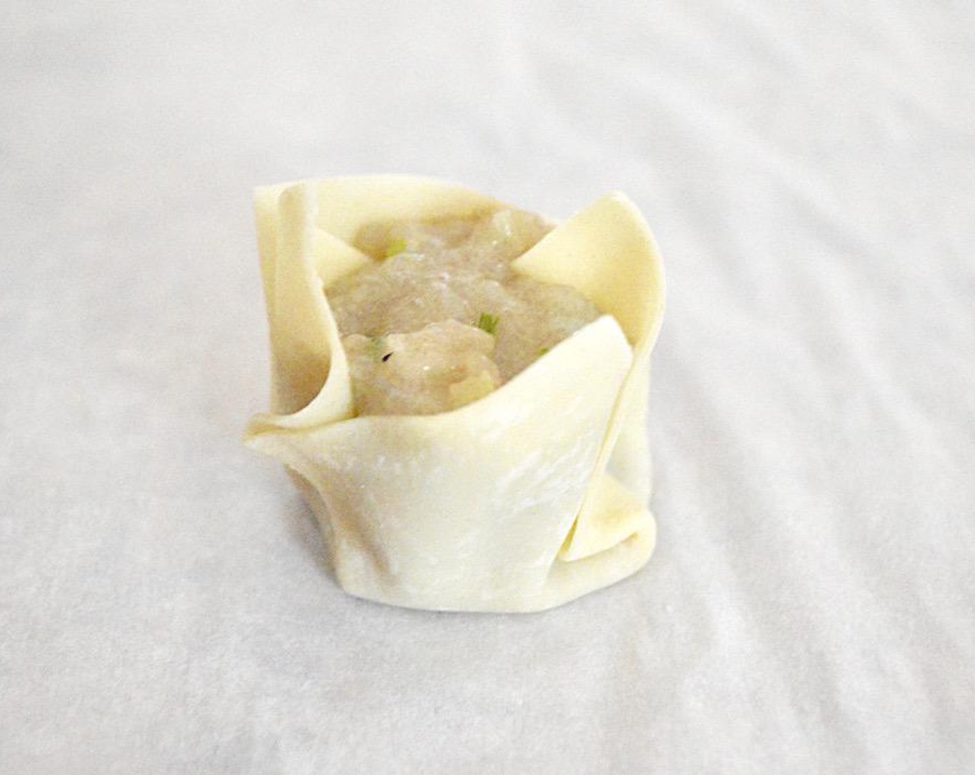 step 2 Dollop 2 teaspoons of that filling into the center of each of the Wonton Wrappers (24), then bring up the sides and pleat them to look like a little drawstring purse. The filling should peek out a little. Place under a clean, wet cotton towel to keep the wrappers from drying out.