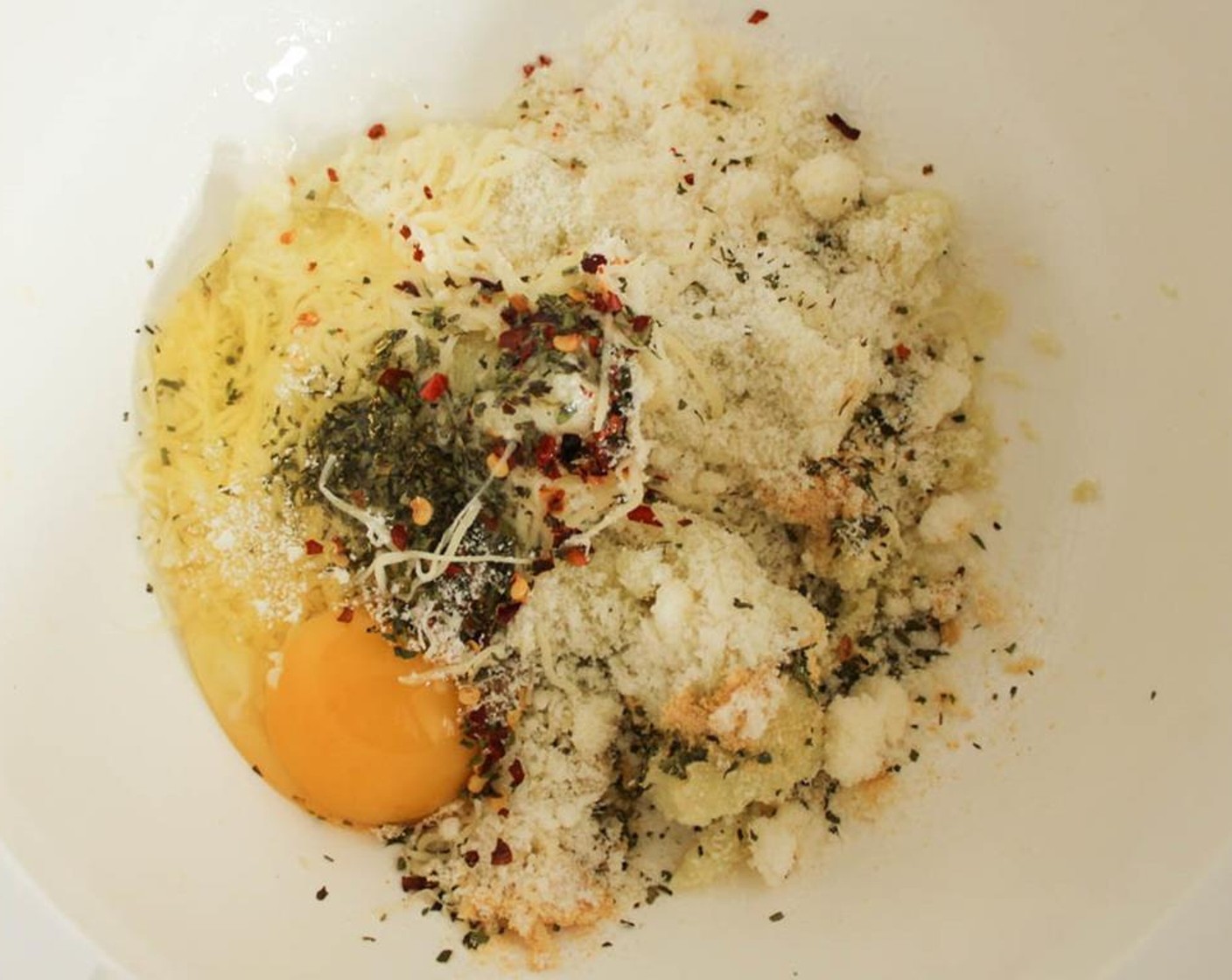 step 6 Place the cauliflower pulp in a mixing bowl and add the Parmesan Cheese (4 Tbsp), Shredded Part-Skim Mozzarella Cheese (4 Tbsp), Dried Oregano (1/2 tsp), Dried Basil (1/2 tsp), Crushed Red Pepper Flakes (1/4 tsp), Salt (1/4 tsp), Simply Organic Garlic Powder (1/2 tsp) and Eggland's Best Classic Egg (1).