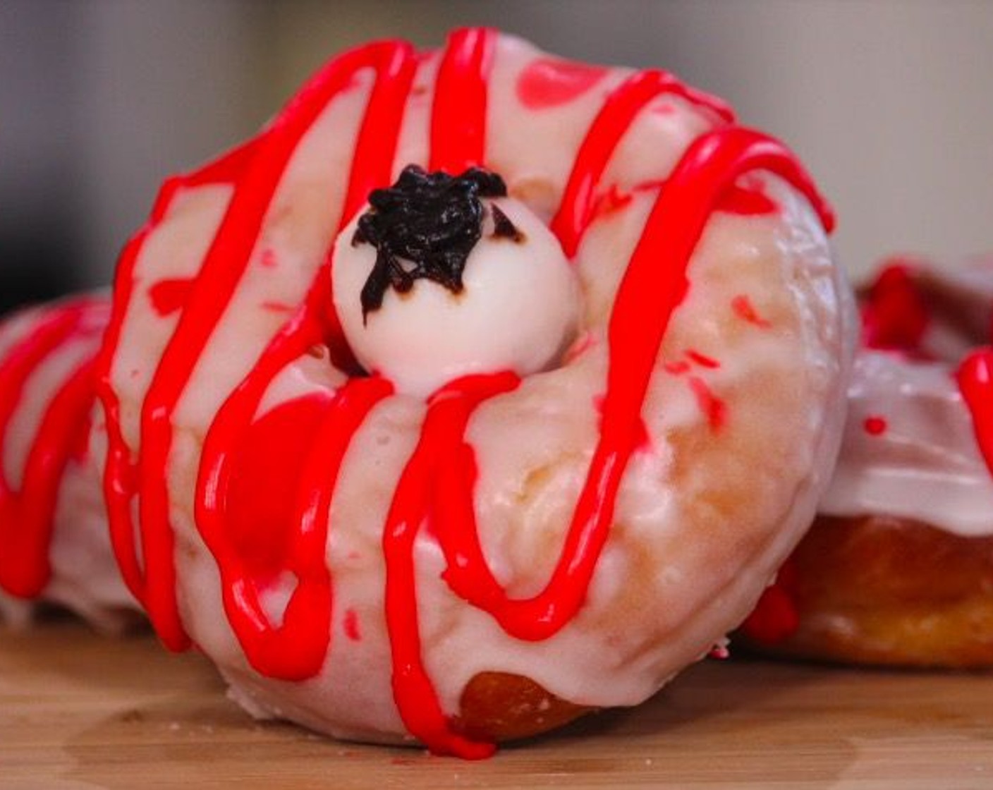 step 15 Pour the remaining red glaze into a piping bag. Pipe drizzle lines over the donuts, then place the gumball in the center. Serve and enjoy!