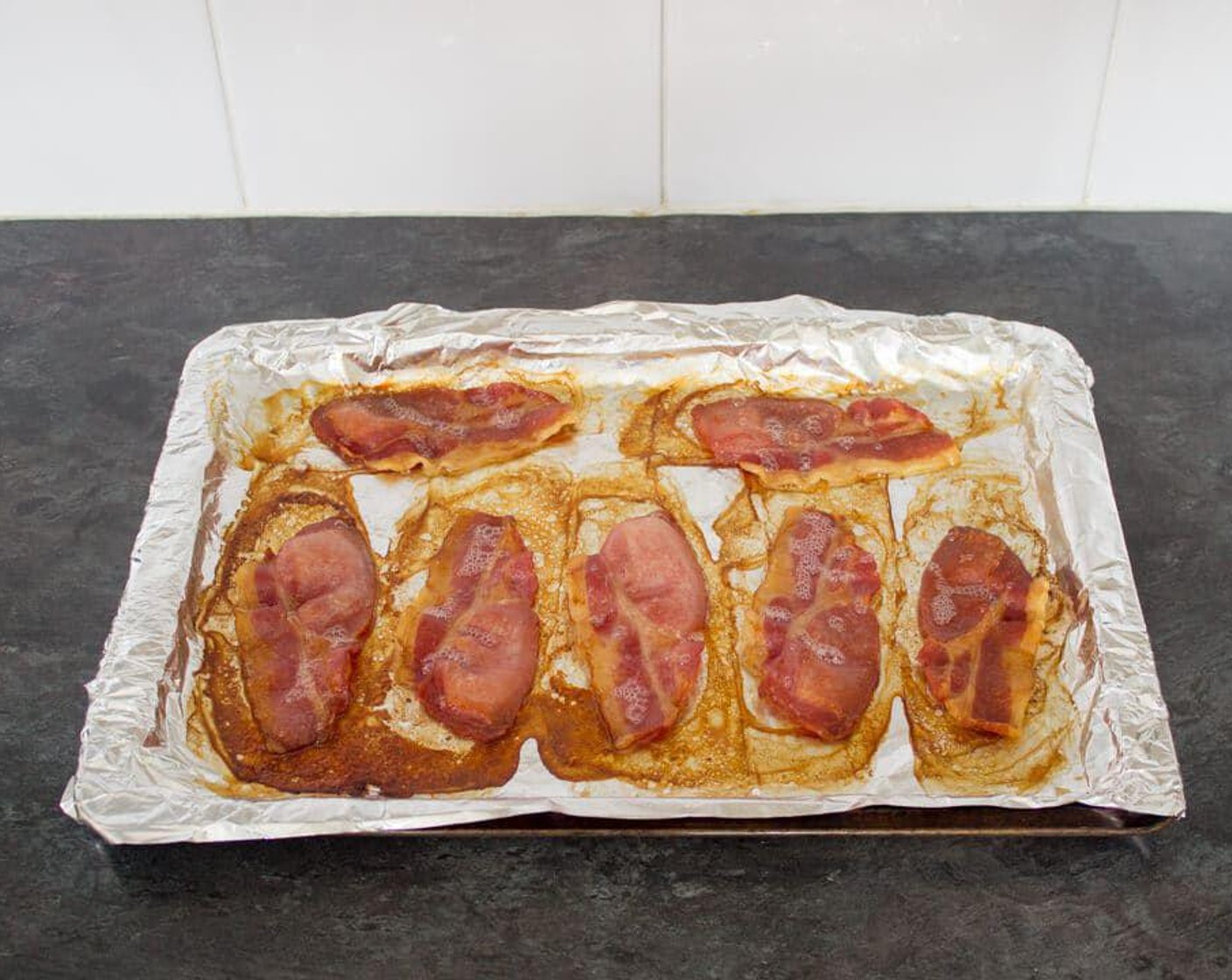 step 2 To cook the bacon, cover a baking tray in foil and evenly lay out the Smoked Bacon (8 slices). Place into the oven to cook until the fat is starting to become crisp, approximately 15-20 minutes. Turn them all over after about 10 minutes to ensure even cooking.