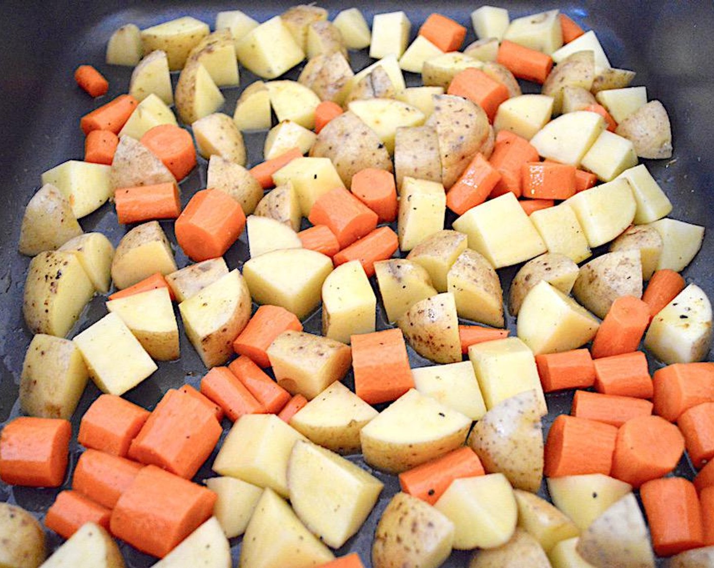 step 2 In a large roasting pan, add the Carrots (7) and Yukon Gold Potatoes (6) into the pan and drizzle them generously with Olive Oil (as needed). Sprinkle them with Salt (to taste), Freshly Ground Black Pepper (to taste), Simply Organic Garlic Powder (1 pinch), and Curry Powder (1 pinch). Toss well to coat the vegetables.