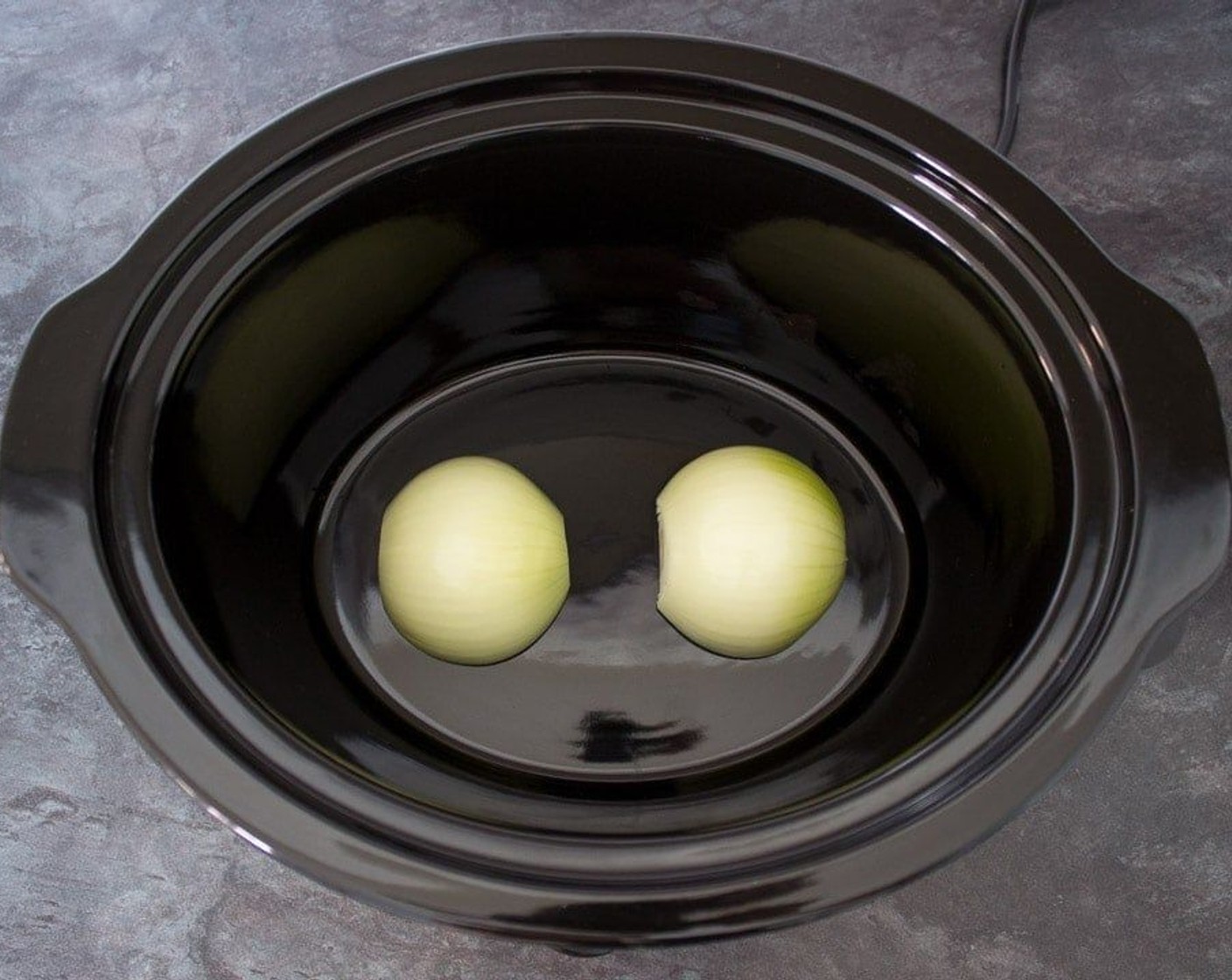 step 2 Peel and slice the Onion (1) in half then place at the bottom of the slow cooker, face down.