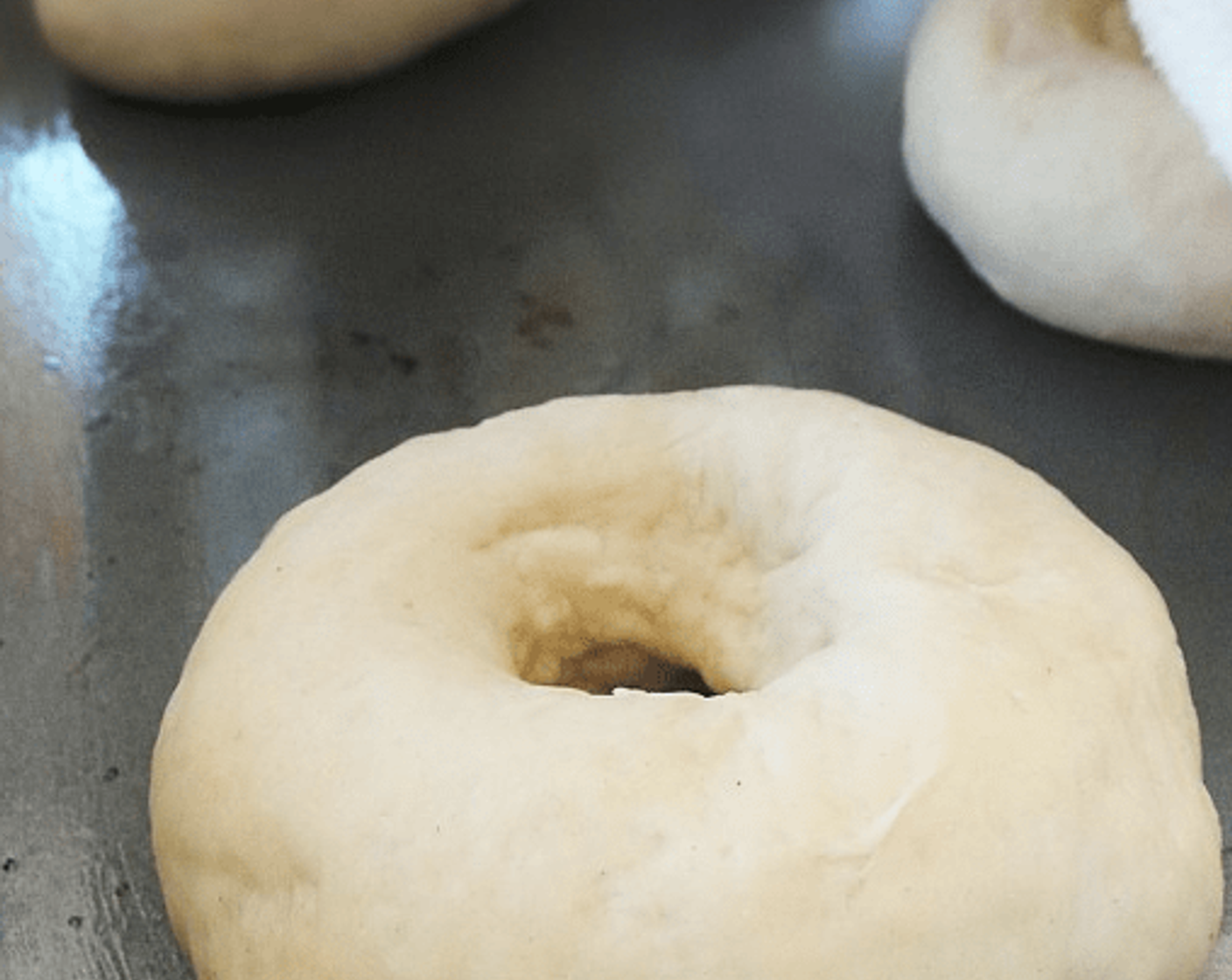 step 7 Coat a finger in flour, and gently press your finger into the center of each dough ball to form a ring. Stretch the ring to about 1/3 the diameter of the bagel and place on a lightly oiled cookie sheet.