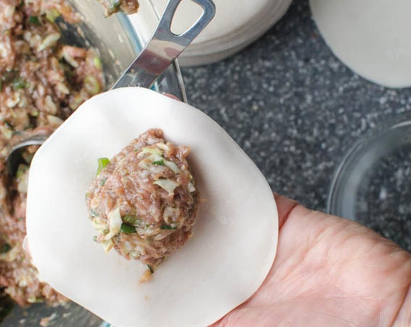 step 4 Add water to a small bowl and have it close by. Hold a Gyoza Wrappers (1 pckg)  in the palm of your hand. Dip your finger into the water and brush the water around the perimeter of the wrapper. Spoon a heaping teaspoon of filling into the center of the wrapper.