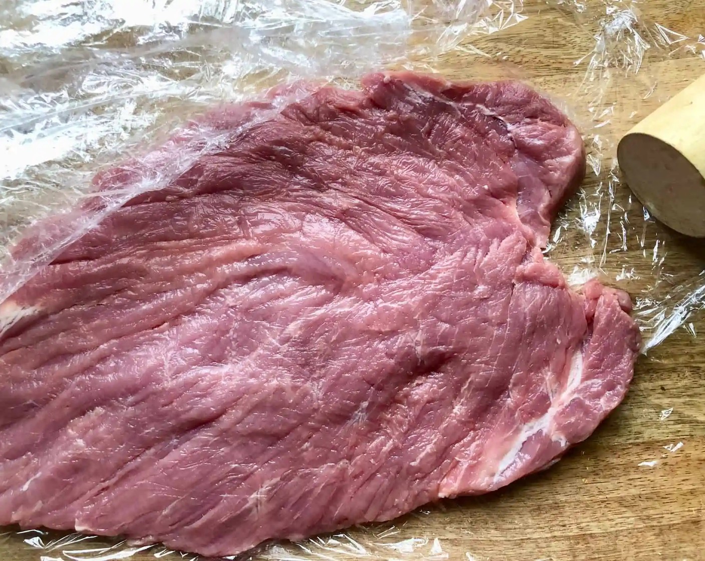 step 3 Pound the Pork Tenderloin: Place the opened piece of meat between two pieces of plastic wrap. Using the flat end of a meat mallet, pound the tenderloin until it is about 1/2-inch thick uniformly. Keep covered with plastic wrap and set aside.