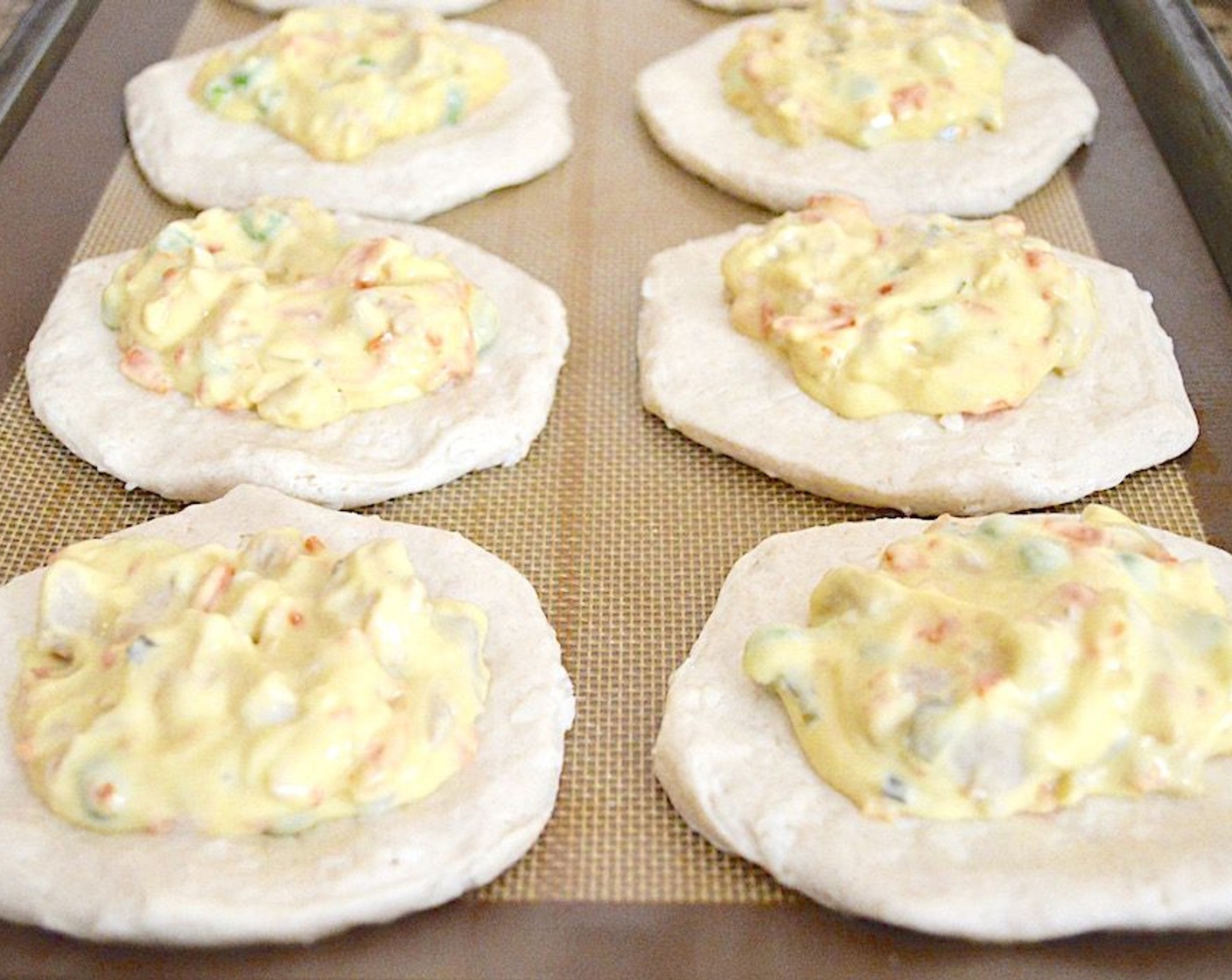 step 6 Take the filling off the heat when it is done and scoop 2 scant tablespoons of it onto the center of each biscuit. Gently pull the sides of the biscuit dough up and over the filling and pinch it all together really well to close it. Flip each one over so that the bombs are seam side down on the sheet tray.