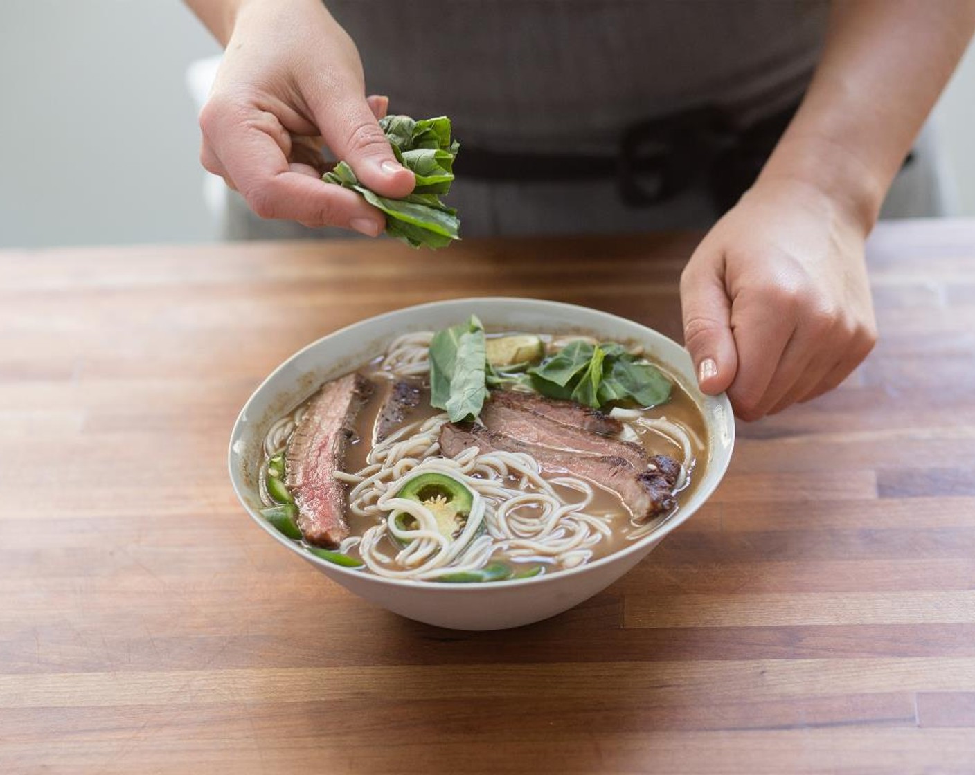 step 16 Place the noodles in the center of two bowls. Top with the sliced onions, jalapenos, and steak. Ladle the broth over all. Top with the basil leaves. Serve with Hoisin Sauce (3 Tbsp), Sriracha (2 Tbsp), and lime wedges.