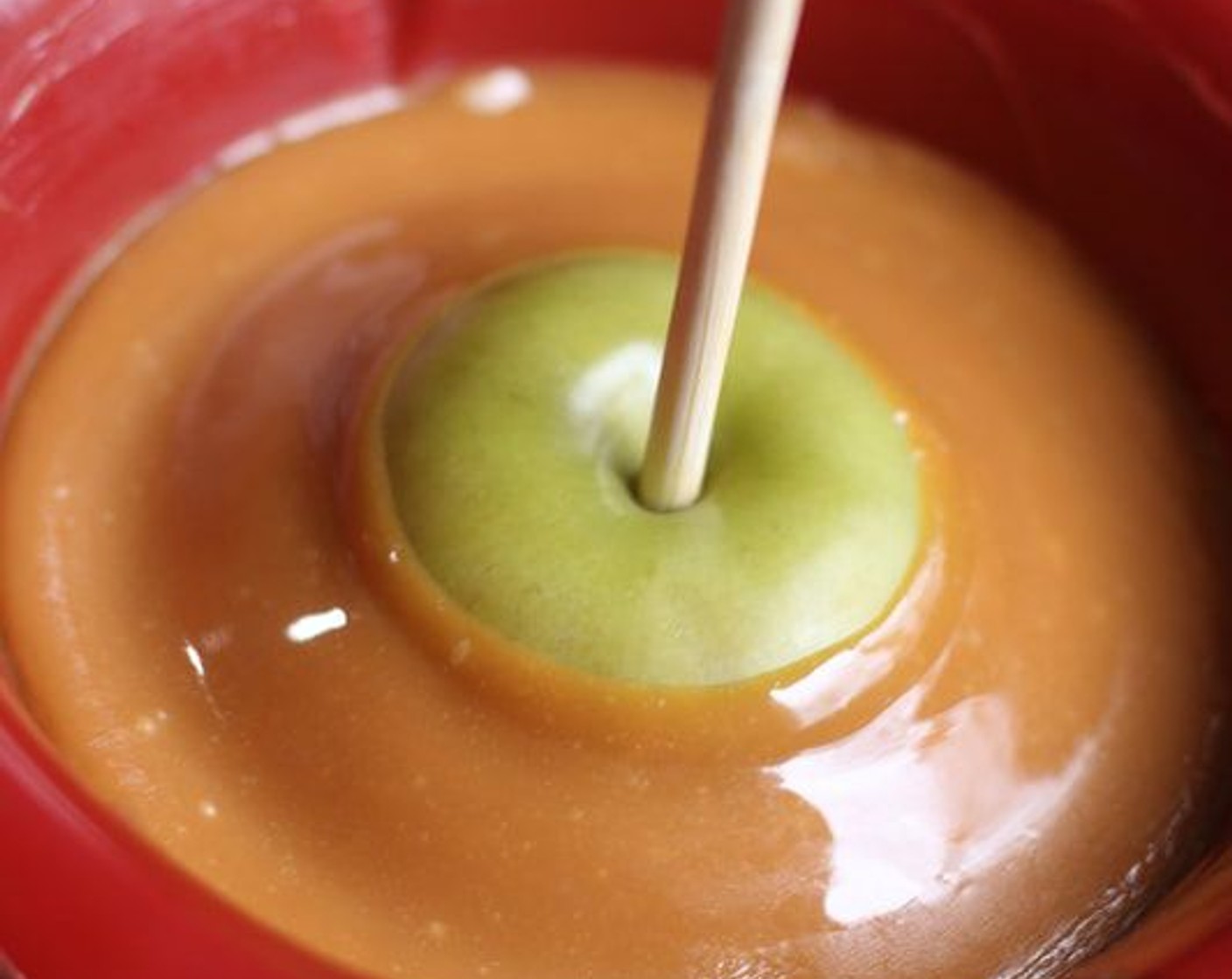 step 9 Dip apples one at a time into caramel on an angle so it covers nearly to the top center. Rotate and turn to coat apple. Lift apple and let excess runoff, then run bottom of apple along the inside edge of the bowl to remove excess caramel. Lift apple and turn apple upside down to let caramel run up the apple a little, hold this way for about 30 seconds.
