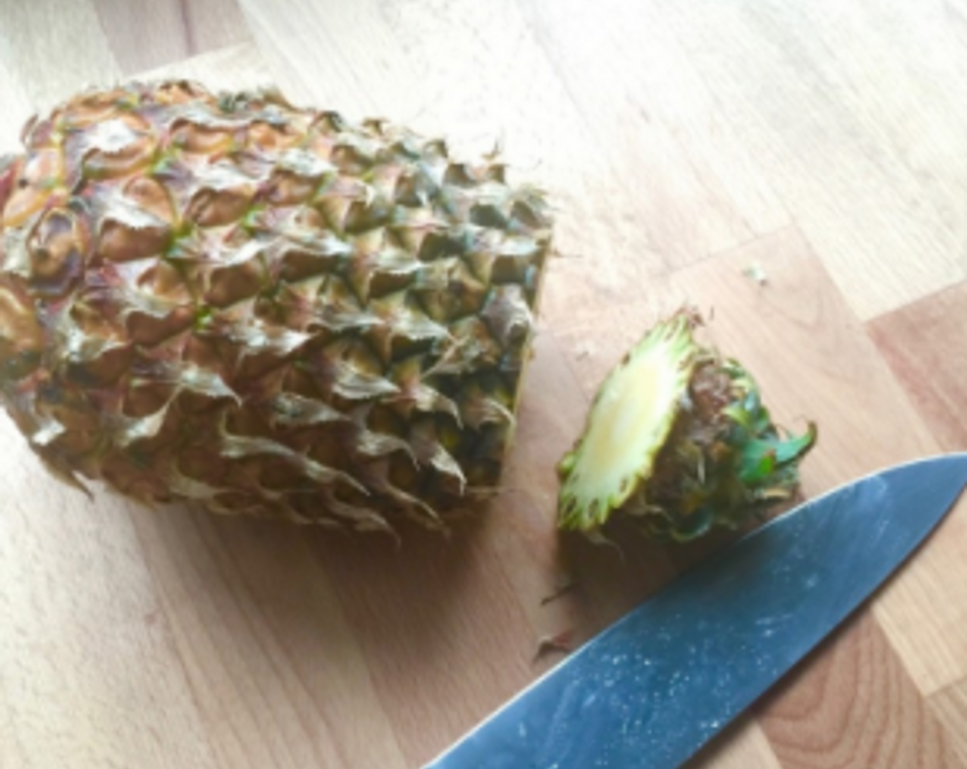 step 4 First, place the pineapple on its sides of a chopping board and slice off the top green crown of the pineapple.