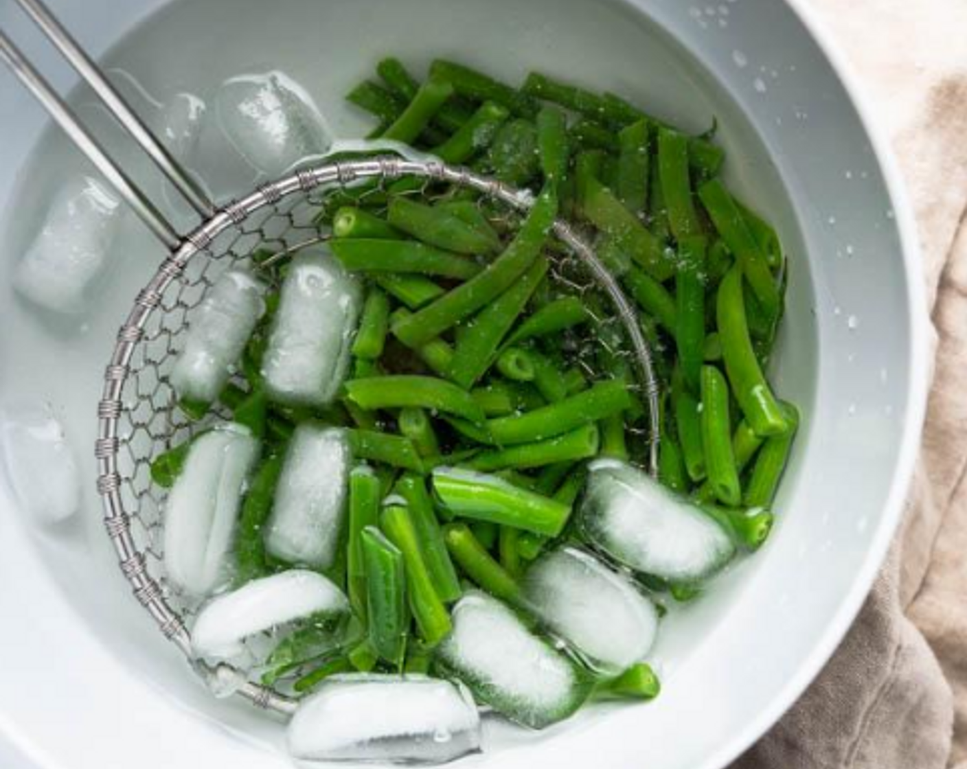 step 6 Use a kitchen spider or slotted spoon to transfer the cooked green beans to the ice bath to stop the cooking and retain the bright green color.