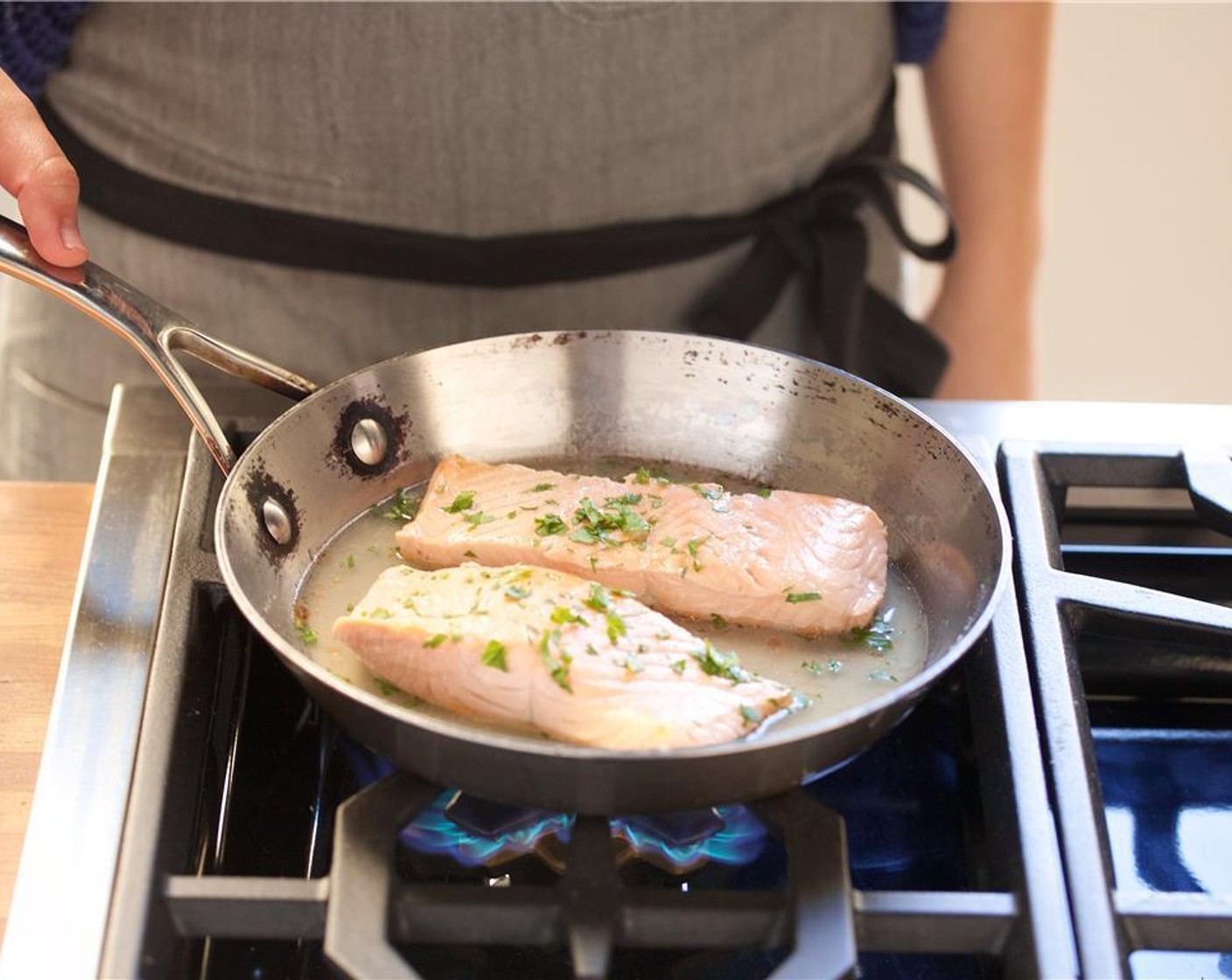 step 4 Heat a medium saute pan over medium heat. Add the White Cooking Wine (1/2 cup) and half a cup of water. Season with Salt (1 tsp) and Ground Black Pepper (1/2 tsp). Add the Salmon Fillets (2) and half of the parsley to the saute pan. Simmer for seven minutes.