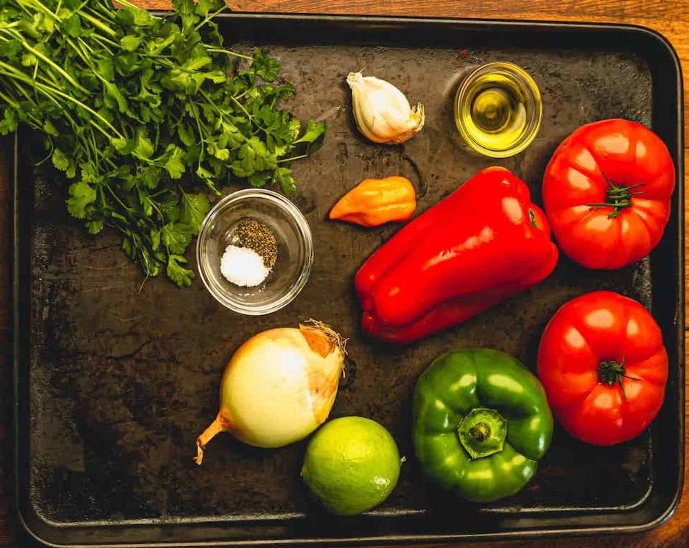 step 2 Cut Beefsteak Tomatoes (2), Red Bell Pepper (1), Green Bell Pepper (1), Habanero Pepper (1), and Yellow Onion (1) in half, place on the baking sheet, and drizzle with Olive Oil (1 tsp).