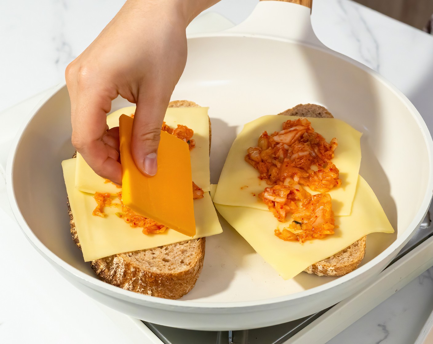 step 2 Heat a large non-stick skillet with a lid over medium heat. Once the pan is hot, place 2 pieces of bread, mayonnaise-side down on the skillet. Top with 2 slices of Gouda (4 slices), 2 Tbsp of Kimchi (1/4 cup), then 2 slices of Mild Yellow Cheddar (4 slices). Put the lid on and cook until the cheese begins to melt and the bottom is golden brown.