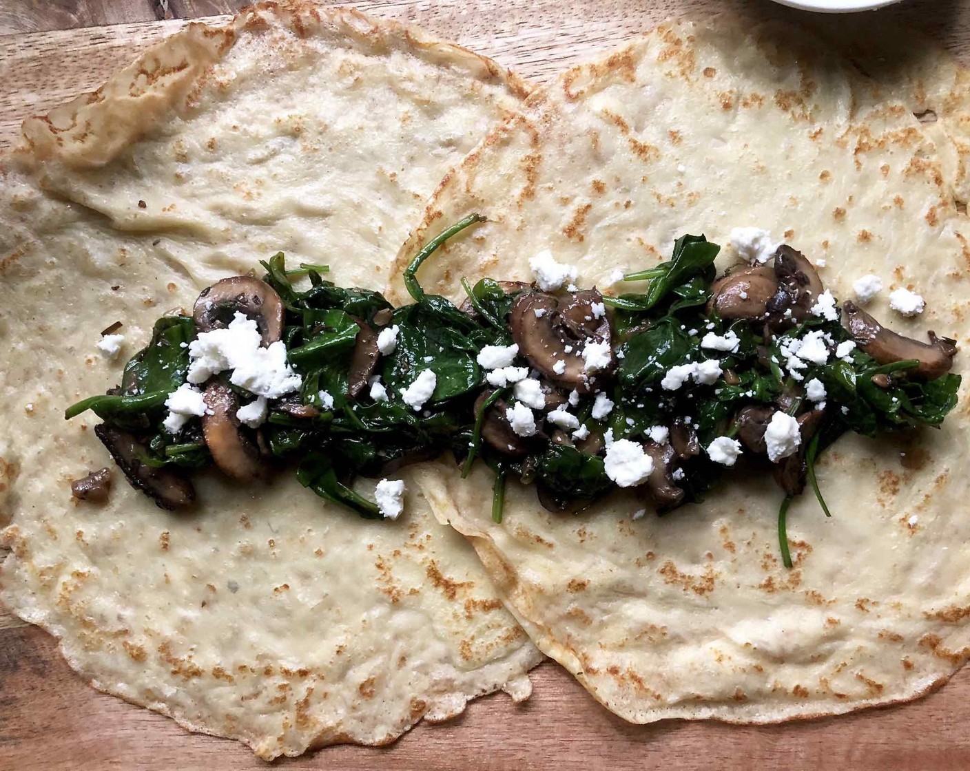 step 9 On a clean work surface, overlay two crepes by 3 inches, then spoon 3 large tablespoons of mushroom mixture in a row in the center of the crepes. Distribute Crumbled Feta Cheese (1/2 cup) on top of the filling.