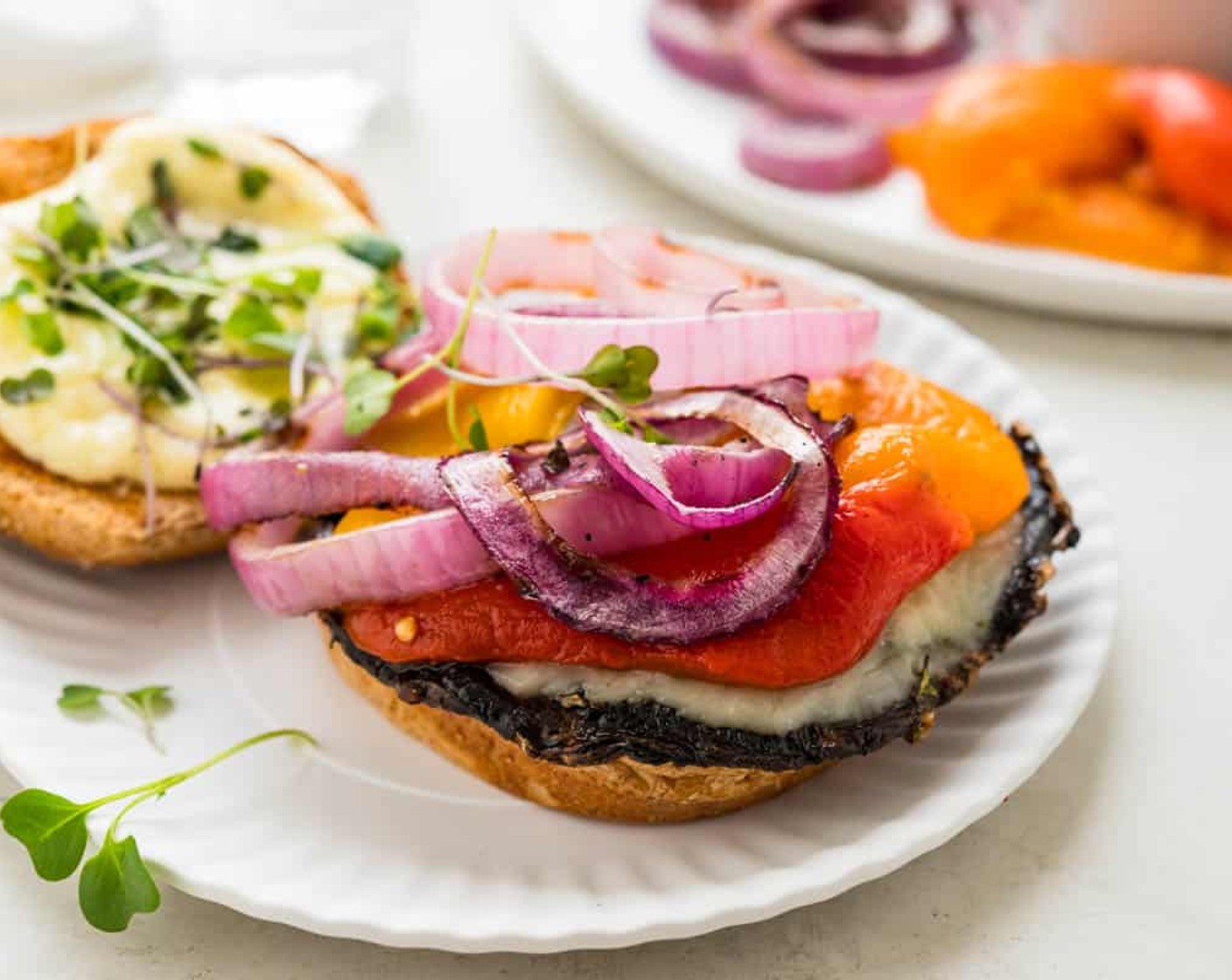 step 15 To assemble the burgers, spread garlic aioli on the top and bottom buns. Place mushrooms on the buns. Top with one or two slices of roasted bell peppers, grilled onions and Microgreens (1 cup) or lettuce. Place the top bun on the mushroom burger and serve.