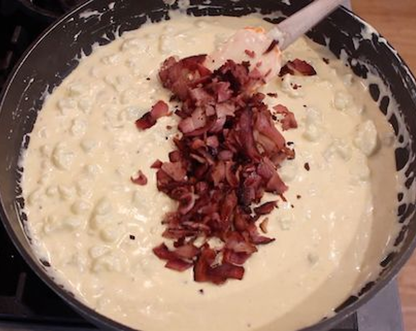step 5 Once the mix has melted down and thickened slightly, drain all the excess water off the cooked cauliflower and add it to the cheese sauce. Mix it together well, then add in the bacon pieces, and again mix everything well for 1-2 minutes.