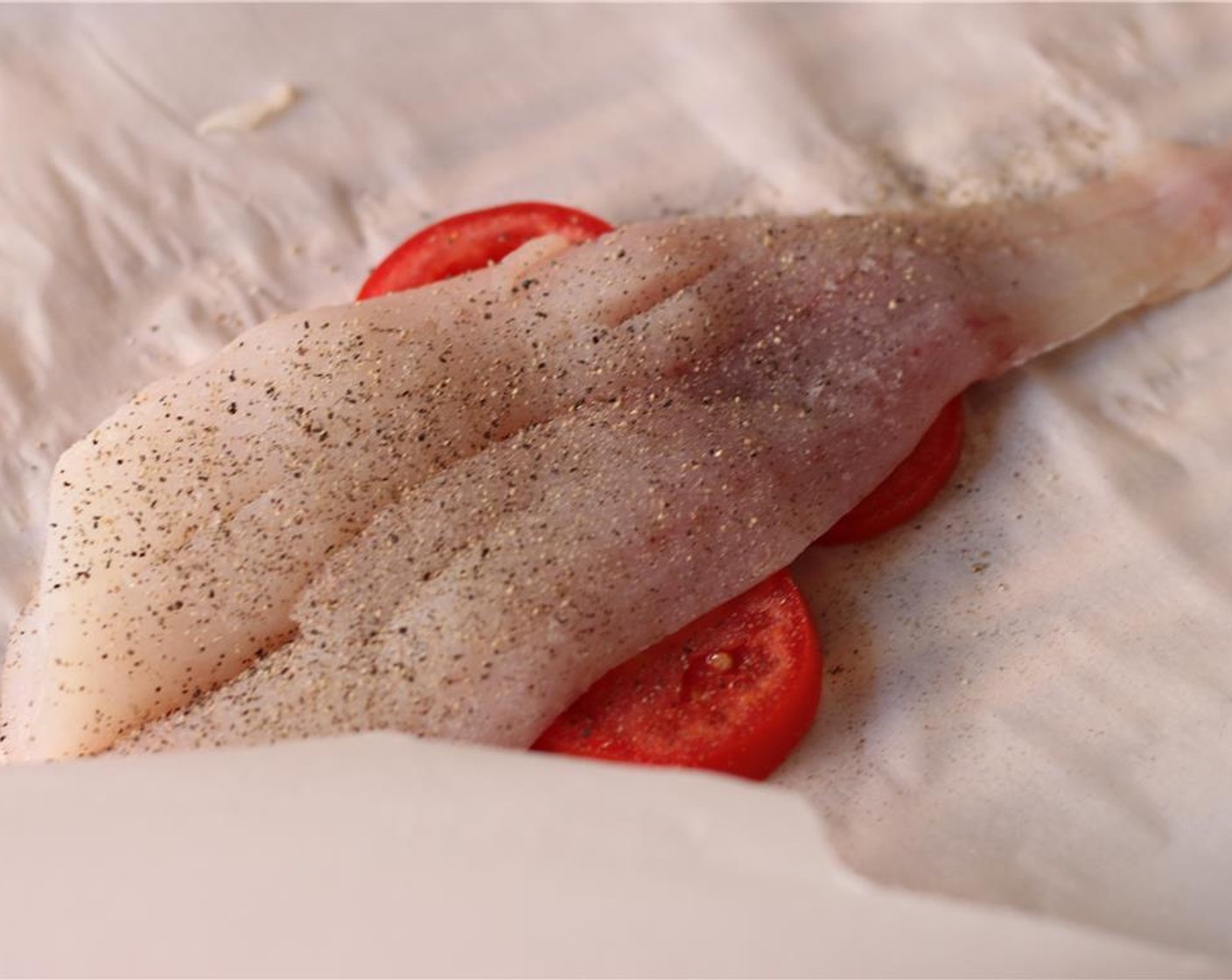 step 5 Place a large piece of parchment paper on a baking sheet. Arrange half the tomato slices in the center of the paper, and place 1 of the Cod Fillets (2) on top. Sprinkle with Salt (to taste) and Ground Black Pepper (to taste).