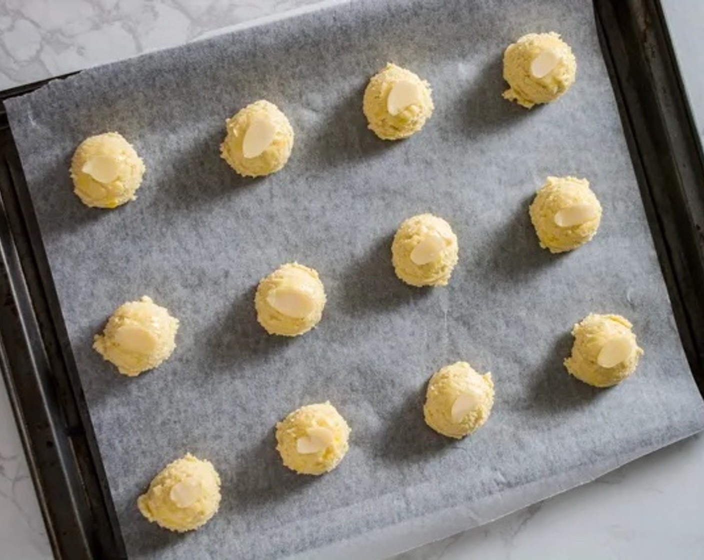 step 6 Line a baking sheet with parchment paper. Scoop heaping tablespoons of the cookie dough onto the sheet, leaving about 2-inches of space in between each cookie. Top each cookie with one of the Sliced Almonds (1/4 cup).