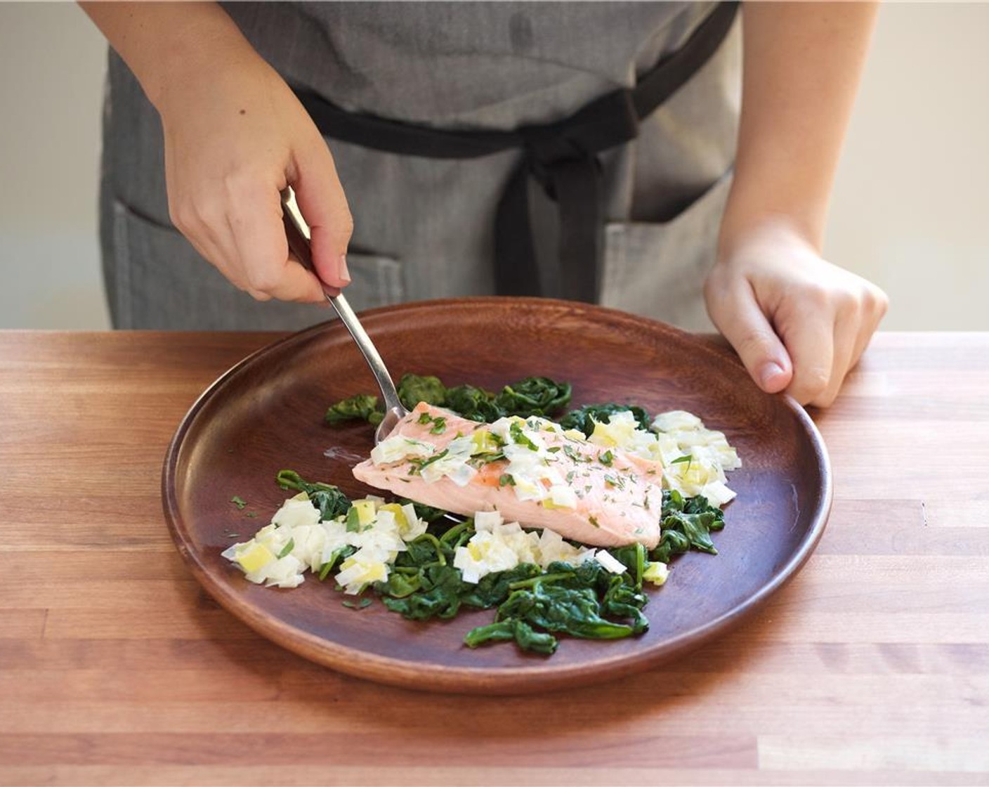 step 8 In the center of two plates, place the spinach. Add the salmon fillets on top of the spinach and top with leek cream sauce. Garnish with remaining parsley.