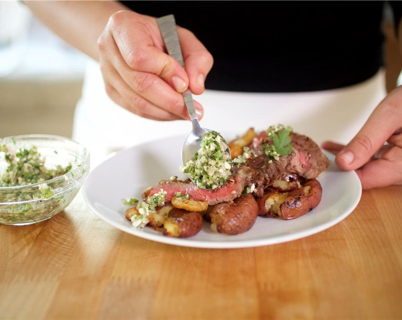 step 10 Cut the steak into 1/4 inch thick slices. Place the potatoes and garlic, down the center in a row between the two plates. Arrange the steak slices fanned over the top of the potatoes. Spoon the chimichurri on top. Garnish with the parsley leaves.