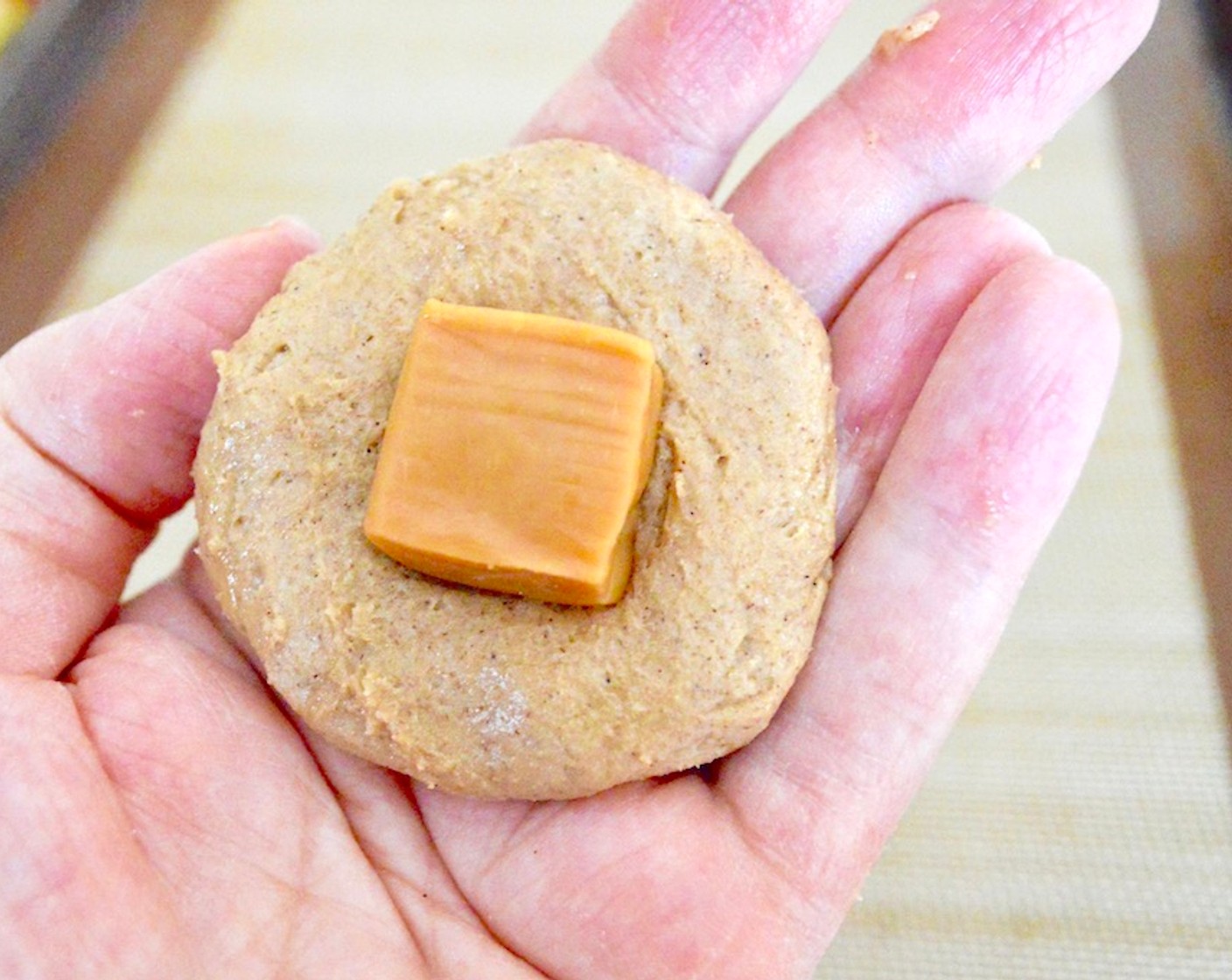 step 8 Then use a 1.5 inch cookie scoop to bring two scoops together into a ball. Flatten it a little into a disc and place one of the Caramel Candies (12) in the center.