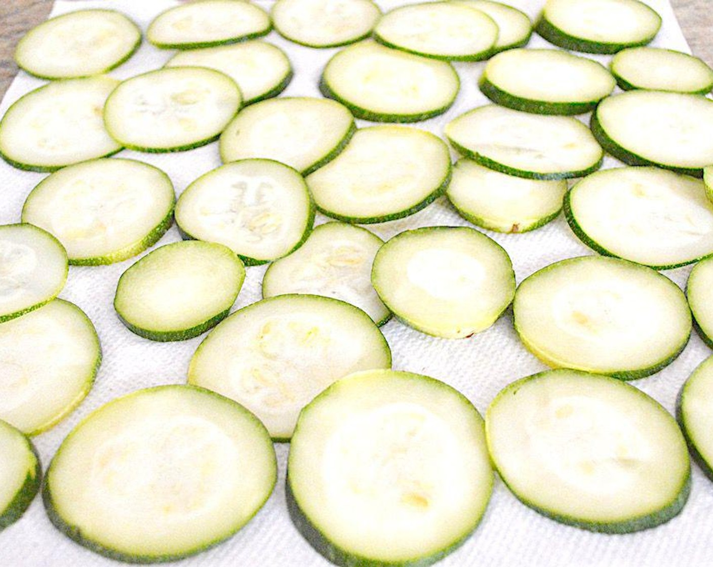 step 2 Use either a very sharp knife or mandolin to slice the Zucchini (1) into really thin discs. Place the slices on paper towels and layer more paper towel on top of them. Press firmly to wring out a lot of the moisture from the slices, which is the enemy in this dish. Then lay them out on the lined sheet trays in a single layer.