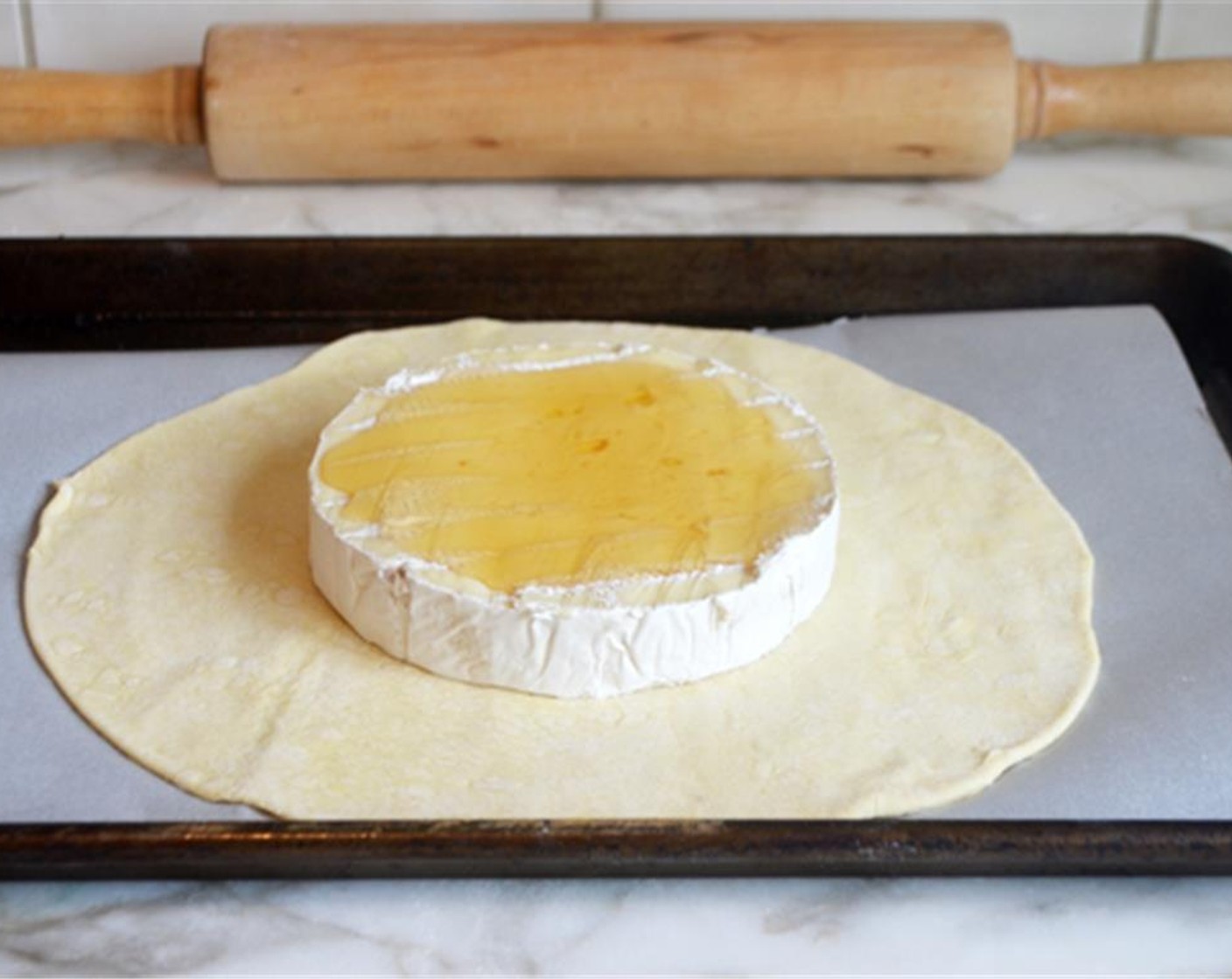 step 3 Place one of the pastry circles on a parchment-lined baking sheet. Cut off the top rind of the Brie Cheese Round (1) and place on top of the pastry. Then drizzle with Honey (2 Tbsp).