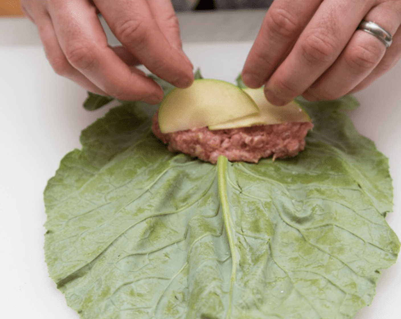 step 7 Place 1 collard leaf on your work surface with the stem end toward you and the dark side facing down. Overlap the cut edges where you removed the stem. Spoon 1/4 of the pork mixture in the center of the leaf, and top with 2 apple slices.