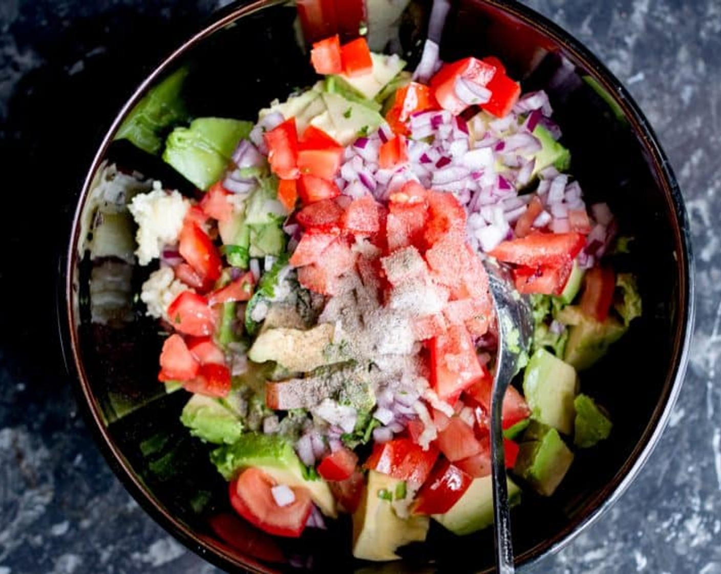 step 2 Place Avocado, Tomato (1), Garlic (1 clove), Chili Pepper (1/2), Red Onion (1/2), 1 Tbsp of Lime (1/2), Extra-Virgin Olive Oil (1 tsp), Salt (1/2 tsp), Ground Black Pepper (1 pinch), and Fresh Cilantro (1 handful) a large bowl and mash everything together with 2 forks until it’s smooth and creamy.