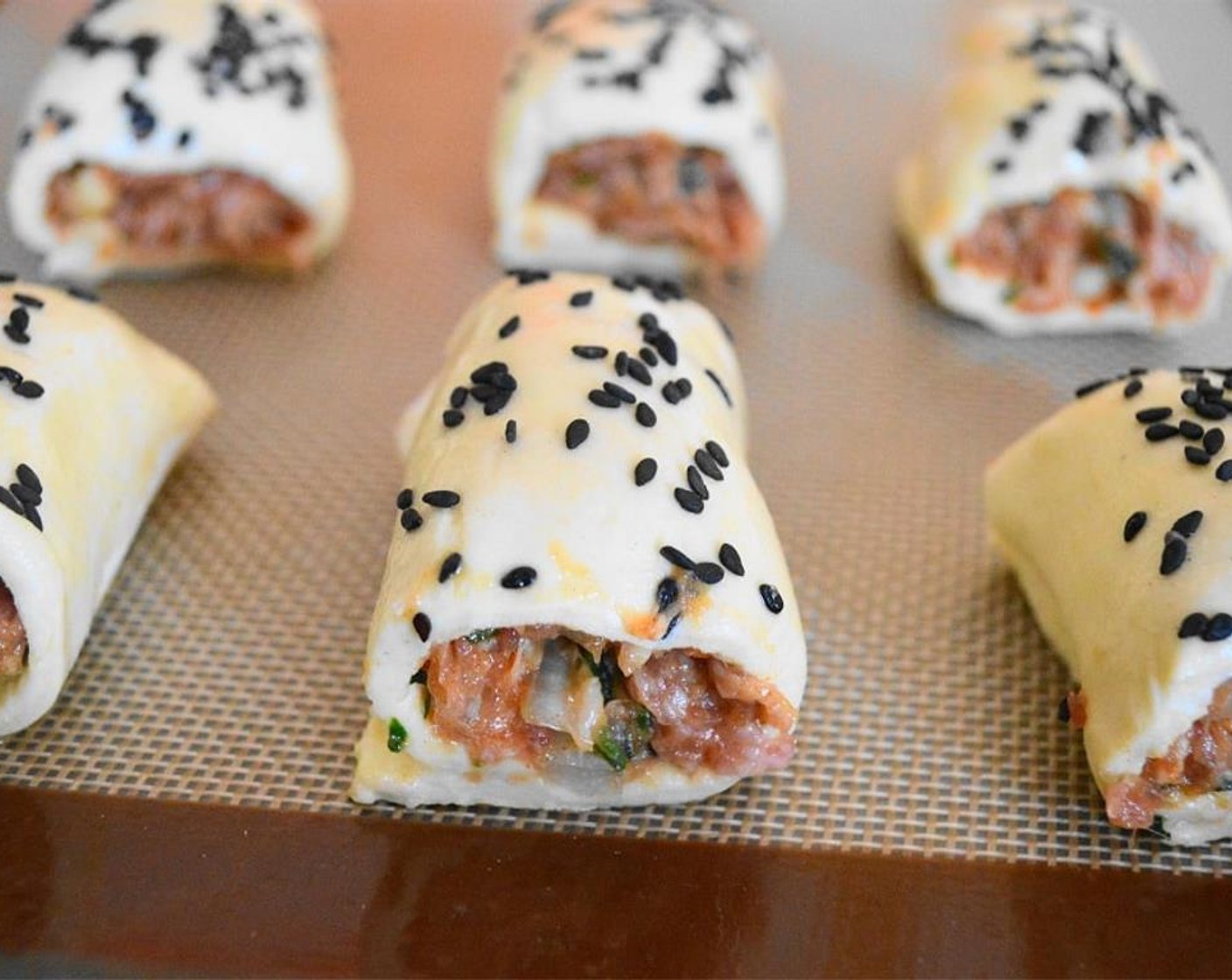 step 6 Roll each puff pasty sheet tightly to surround the sausage log. Then, brush each roll with egg wash, and sprinkle them with the Black Sesame Seeds (to taste).