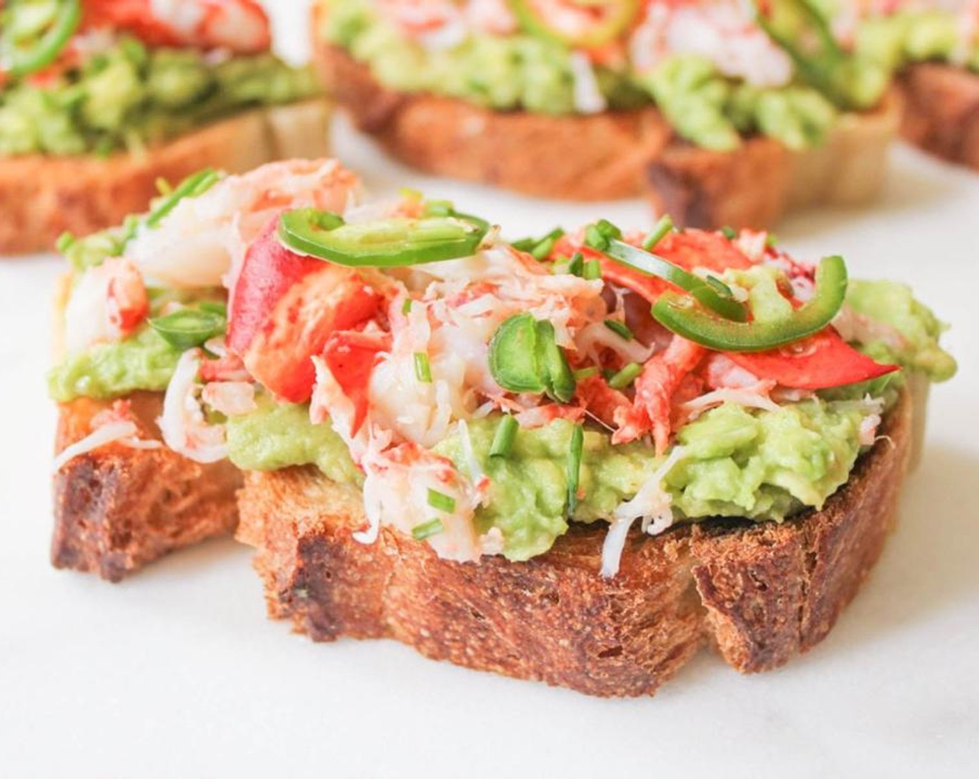 step 6 Spread each piece of toast with a thick layer of avocado mash. Top with the chopped lobster meat, then sprinkle with Jalapeño Pepper (1) and Fresh Chives (1/2 Tbsp). Drizzle each with a little bit of Extra-Virgin Olive Oil (to taste).