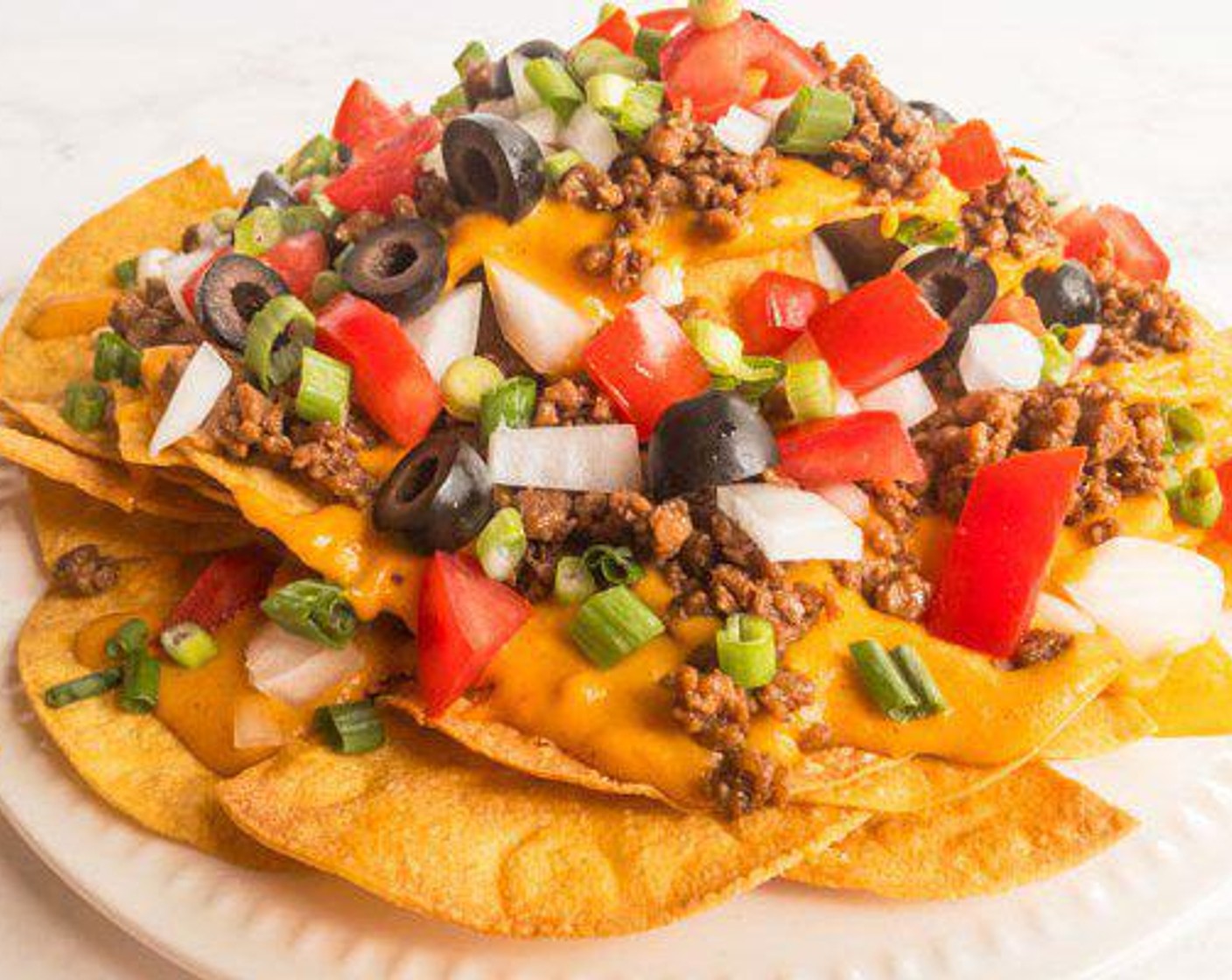 step 7 To assemble nachos, layer half of tortilla, beef, Vegan Nacho Cheese Sauce (1 1/2 cups), Tomato (1), Onion (1/2), repeat layers and garnish with Scallion (1 stalk) and Black Olives (to taste) on top.