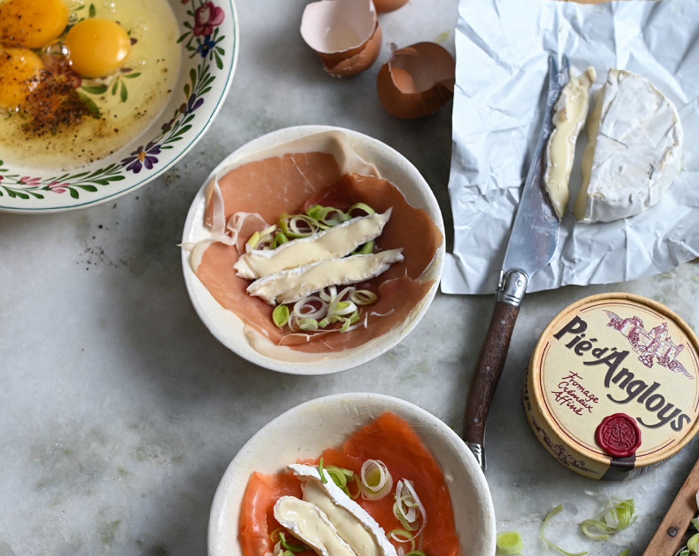 step 2 Grease the ramekins with a little Butter (as needed). Layer the slices of Serrano Ham (3 slices) in one ramekin and Smoked Trout (3 slices) in the other and add two slices of Camembert (1/3 cup) to both.