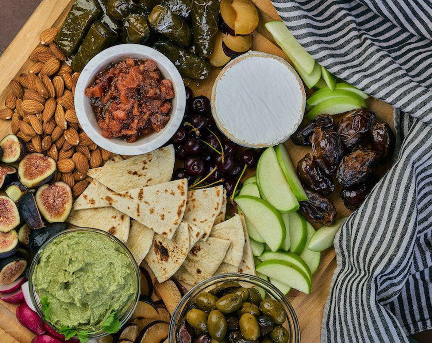 step 1 Place your Hummus (to taste), {@11:}, and Olives (1 2/3 cups) in small bowls. Disperse the Canned Stuffed Grape Leaves (1 2/3 cups), Apples (2), Goat Cheese (2/3 cup), Flatbread (8), Plums (2), Cherry (1 cup), Almonds (1 cup), Dried Dates (8), and {@10:} on a large, wooden board. See photo for inspiration.