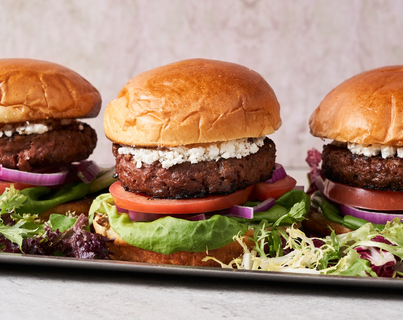 step 4 Spread the cilantro sauce mixture over the bottom buns, then place Lettuce (to taste), Red Onions (to taste), Tomatoes (to taste), patty, and top with Crumbled Feta Cheese (to taste). Cover the burger stacks with the top buns and enjoy immediately!