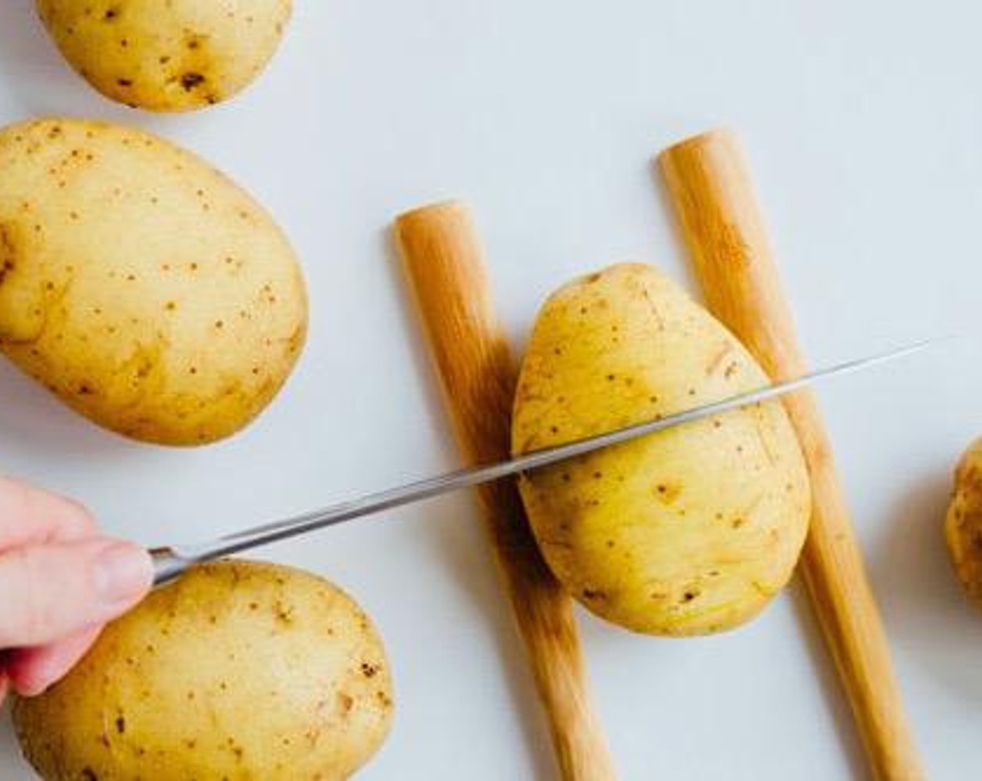 step 1 Lay each of the Yukon Gold Potatoes (2) facedown on its flattest side, setting two wooden spoons on either side to prevent from cutting all the way through, then thinly slice the potato.