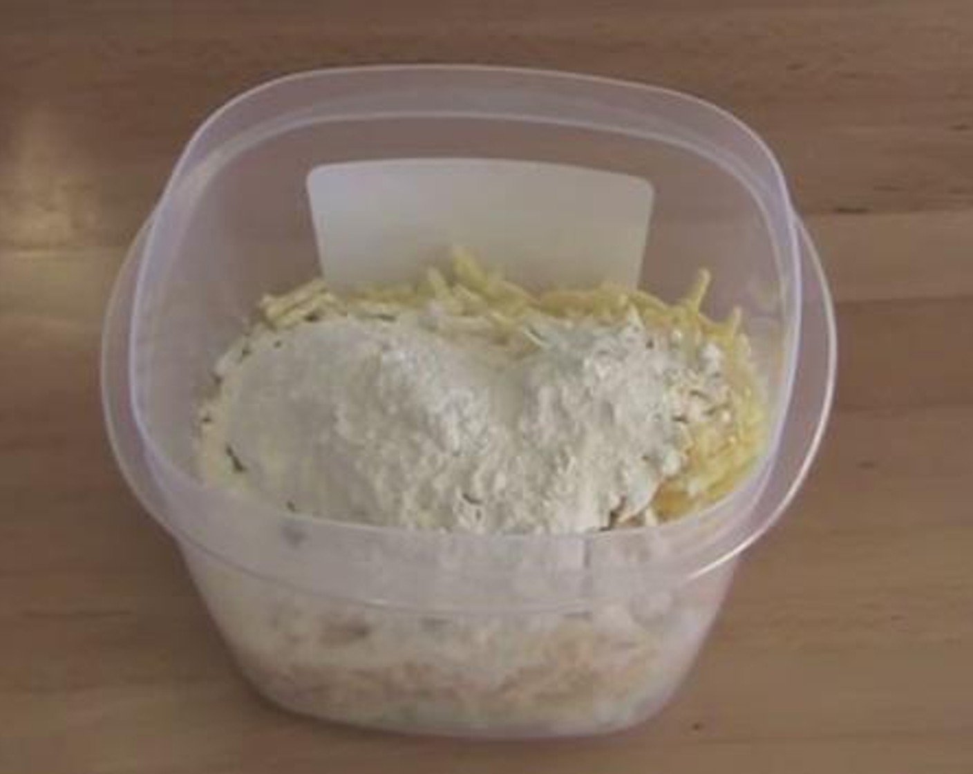 step 2 Inside a plastic container, add the Yellow Onion (1), Ham (1 cup), Cheddar Cheese (1/2 cup), and Self-Rising Flour (1/2 cup). Put on the lid over the container and shake until everything is mixed well.
