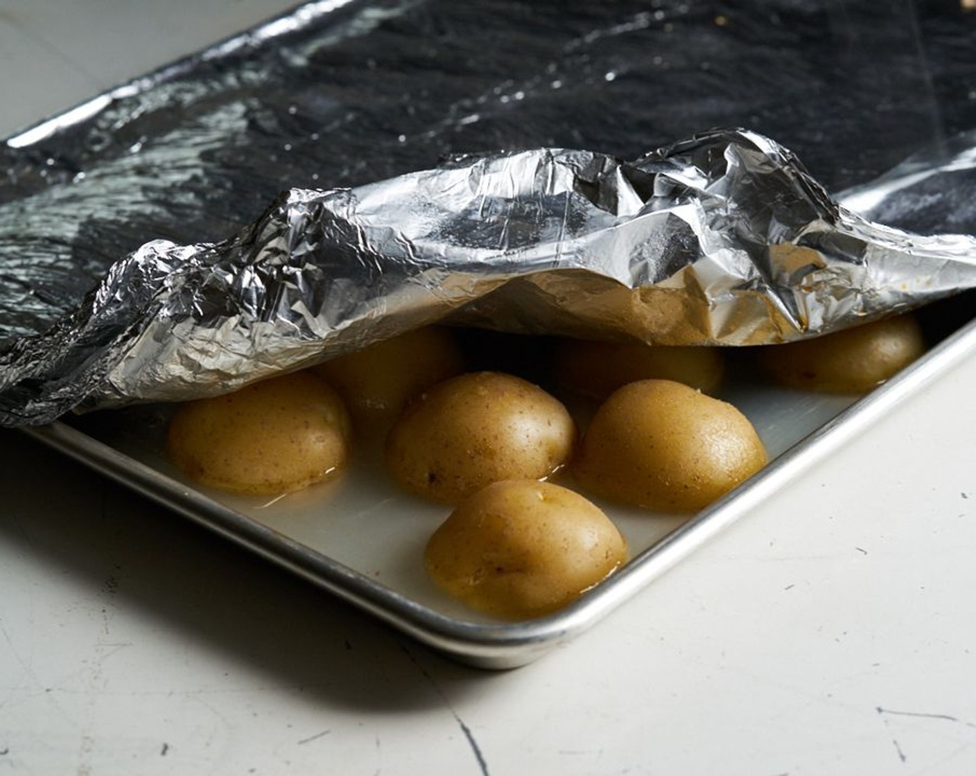 step 3 Add the Water (1 1/2 cups), enough to cover the entire surface of the pan, but you don’t want it to slosh over the sides when you move the pan. Cover the entire pan tightly with foil, you might need two layers. You want to keep all the steam in, so make sure there are no gaps or openings. Bake about 25-30 minutes, until a skewer or knife slides through easily. Check a couple of the potatoes to be sure they are done.