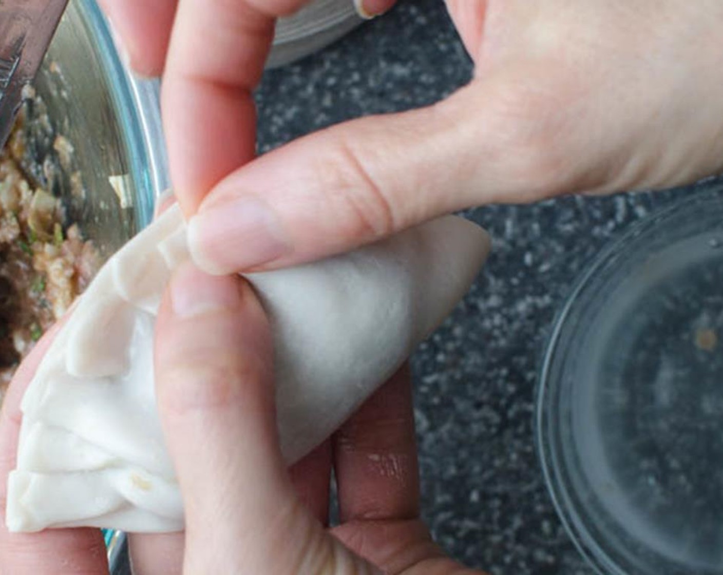 step 5 Fold dumpling in half. Begin pleating the dumpling by making a small fold at the edge of the top wrapper and pressing the pleat firmly to adhere to the bottom of the dumpling. Continue to pleat and press until the dumpling resembles a half-moon and the filling is sealed inside.