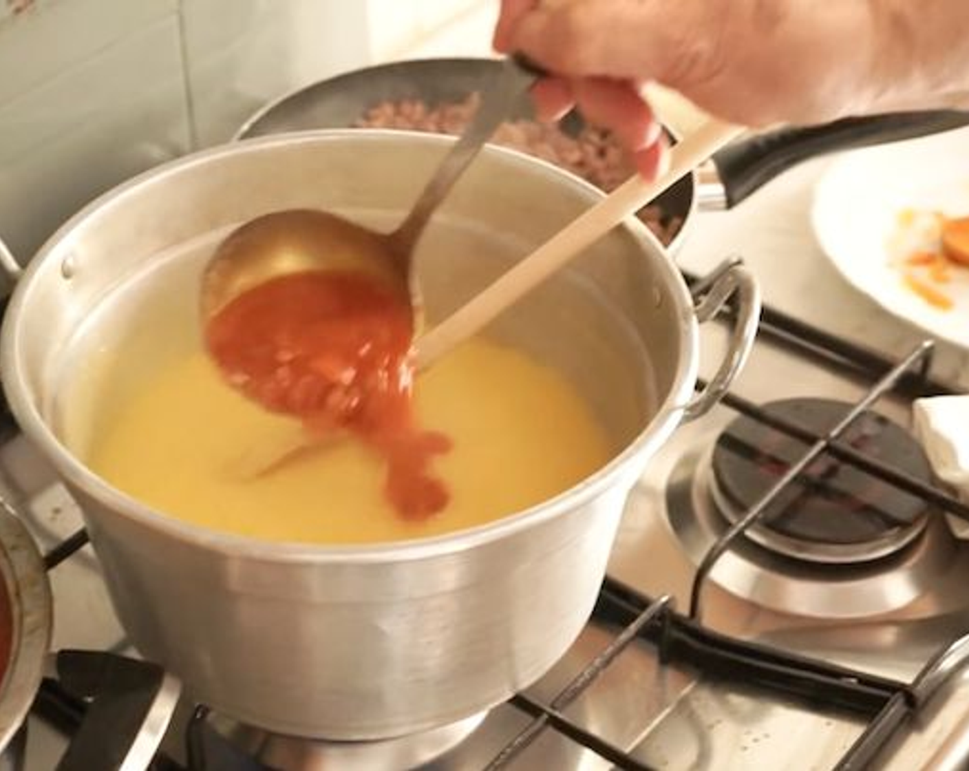 step 9 Using a ladle, pour a portion of the sauce you prepared earlier, into the cornmeal polenta, and mix it through. At the same time add half of the sausage mince you also prepared and stir it in.