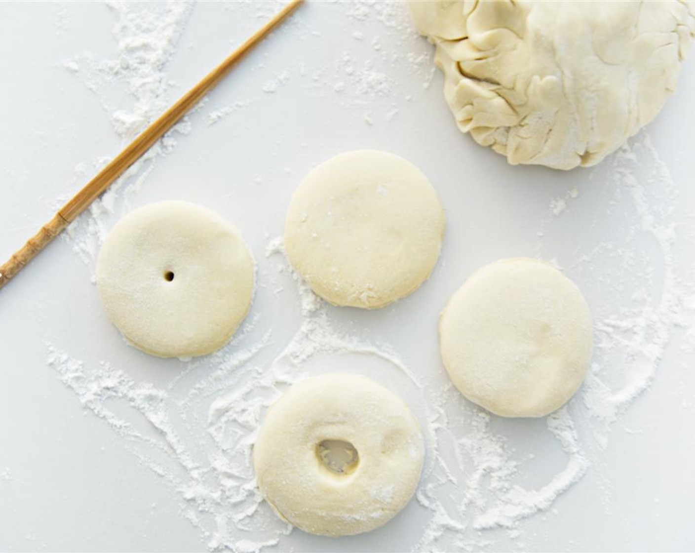 step 6 With a floured cutter or a round glass, cut the rolled dough into doughnuts. Use a chopstick to make the holes by sticking it in the center and swirling until the hole is 1 to 2 inches wide. Gather the scraps and recombine them into the dough for more doughnuts.