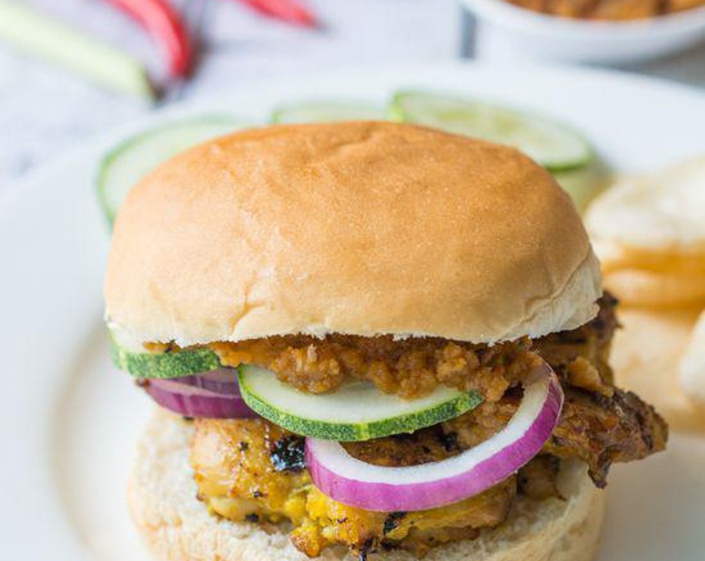 step 5 Now it’s time to assemble the burger! Place the grilled satay chicken on the bottom Hamburger Buns (8), Red Onion (1), and Cucumber (1). Smear with Spicy Peanut Satay Sauce.