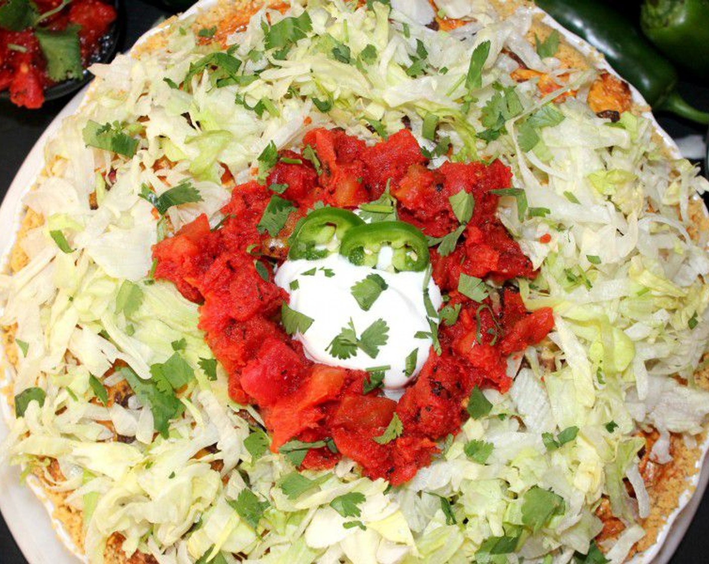 step 11 Now, top it with the Sour Cream (1 cup), Fresh Cilantro (to taste), more queso fresco cheese, Jalapeño Pepper (1/2), Lettuce (to taste), some crumbled chips, and Canned Diced Tomatoes (1/4 cup). Serve with some Hot Sauce (to taste).