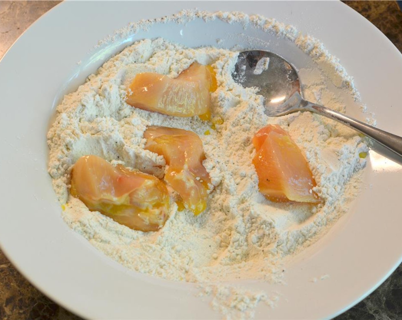 step 5 In small batches of 3 to 4 pieces, coat the egg drenched chicken pieces in the seasoned flour and place them on a foil lined baking sheet.