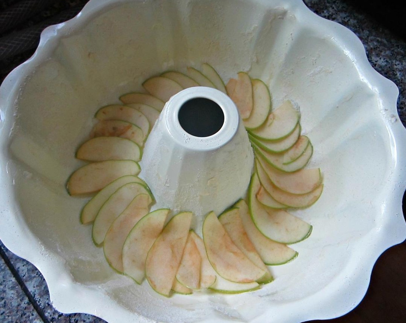 step 3 Take one quarter of a Granny Smith Apples (2) and run it through the mandoline or slice it very fine. Lay this quarter into the bottom of the prepared bundt pan in a fan to top your lovely cake.