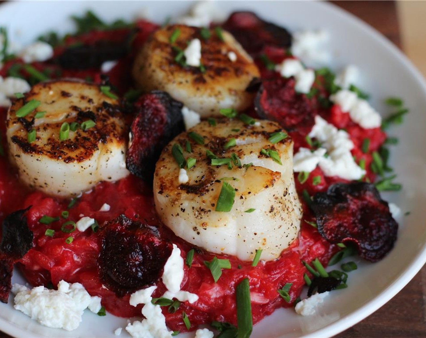 step 17 To plate the dish, spread a cup of risotto on a plate, and top with 3 scallops. Garnish with fresh Goat Cheese (1/2 cup), Fresh Chives (to taste) and beets chips.